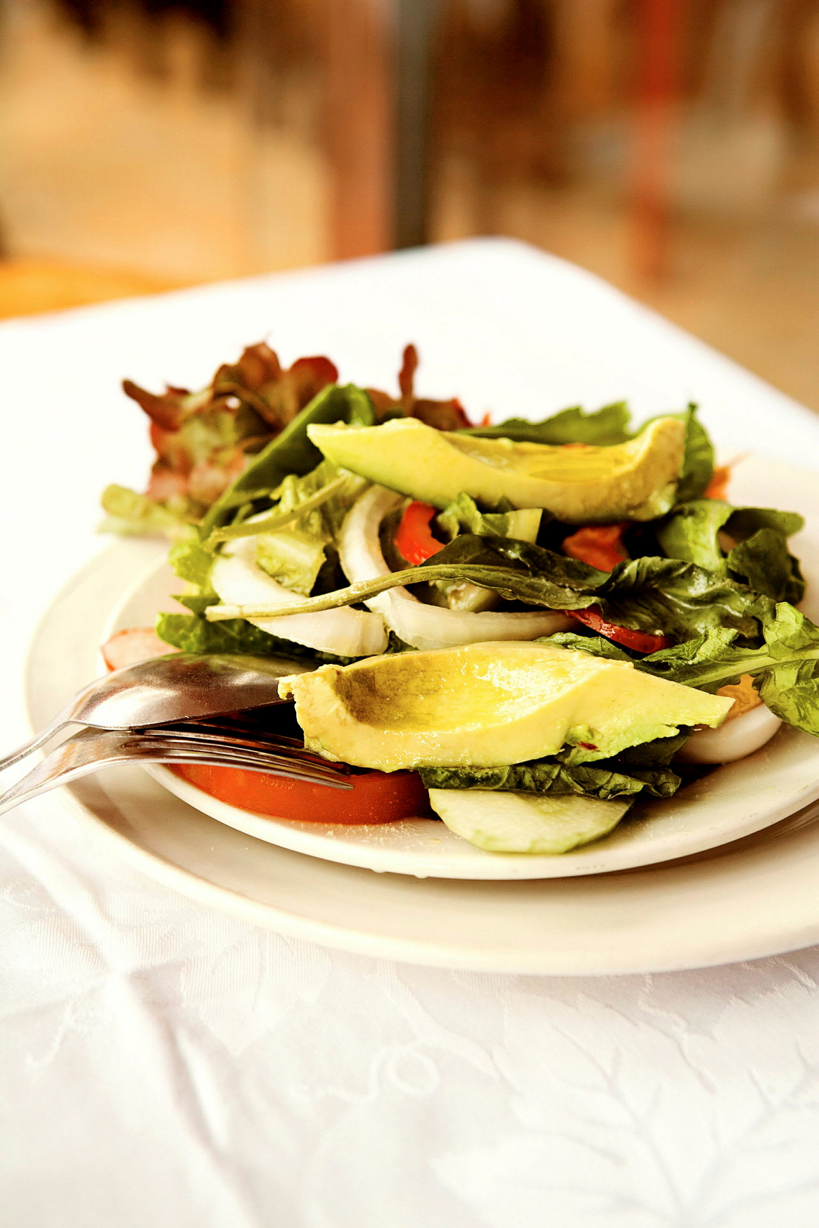 En sallad med avokado, tomater, lök och bladgrönsaker serverad på en tallrik. (AI-genererad text)