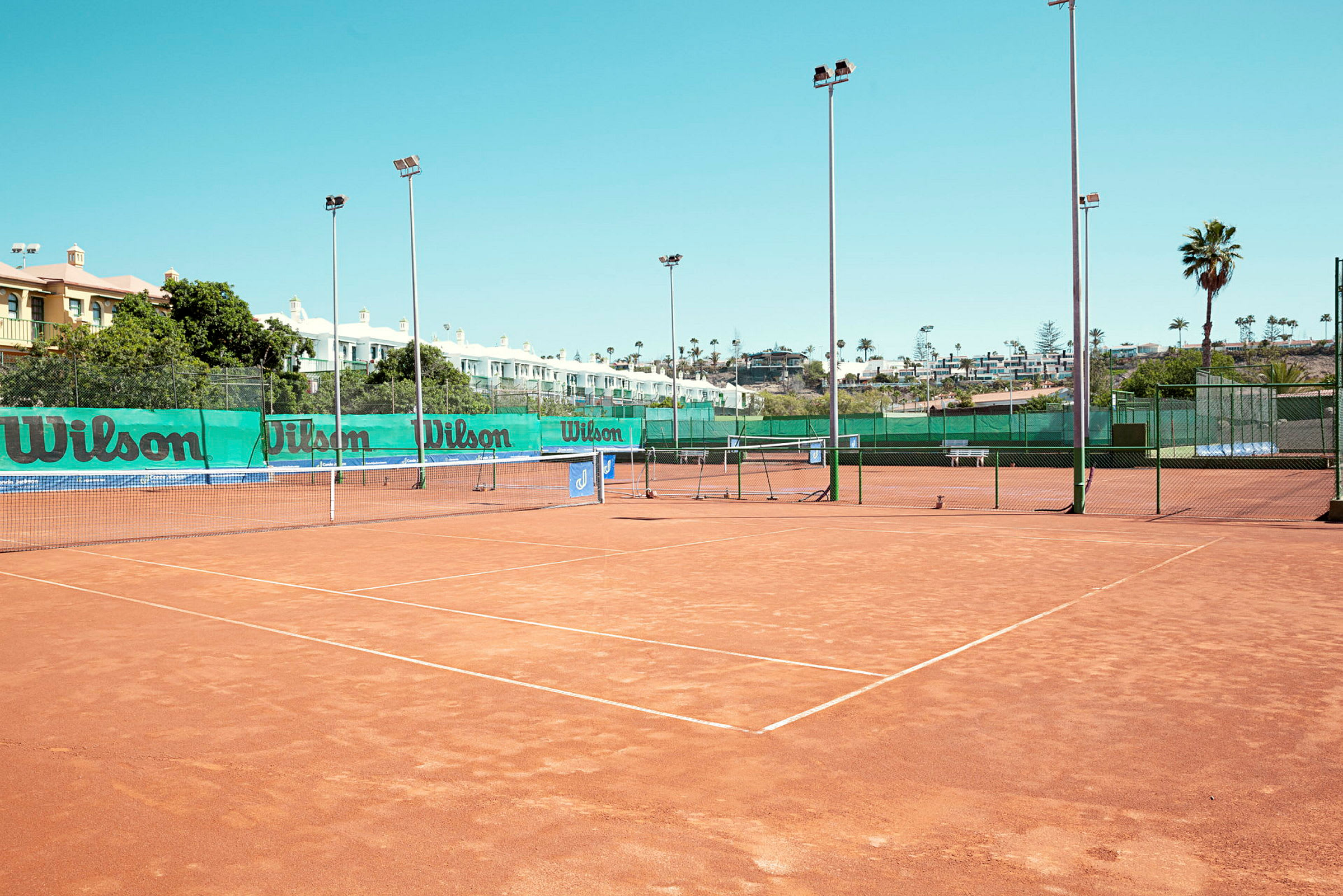 Tennisbanor med grusunderlag, omgivna av nät och lampstolpar. (AI-genererad text)