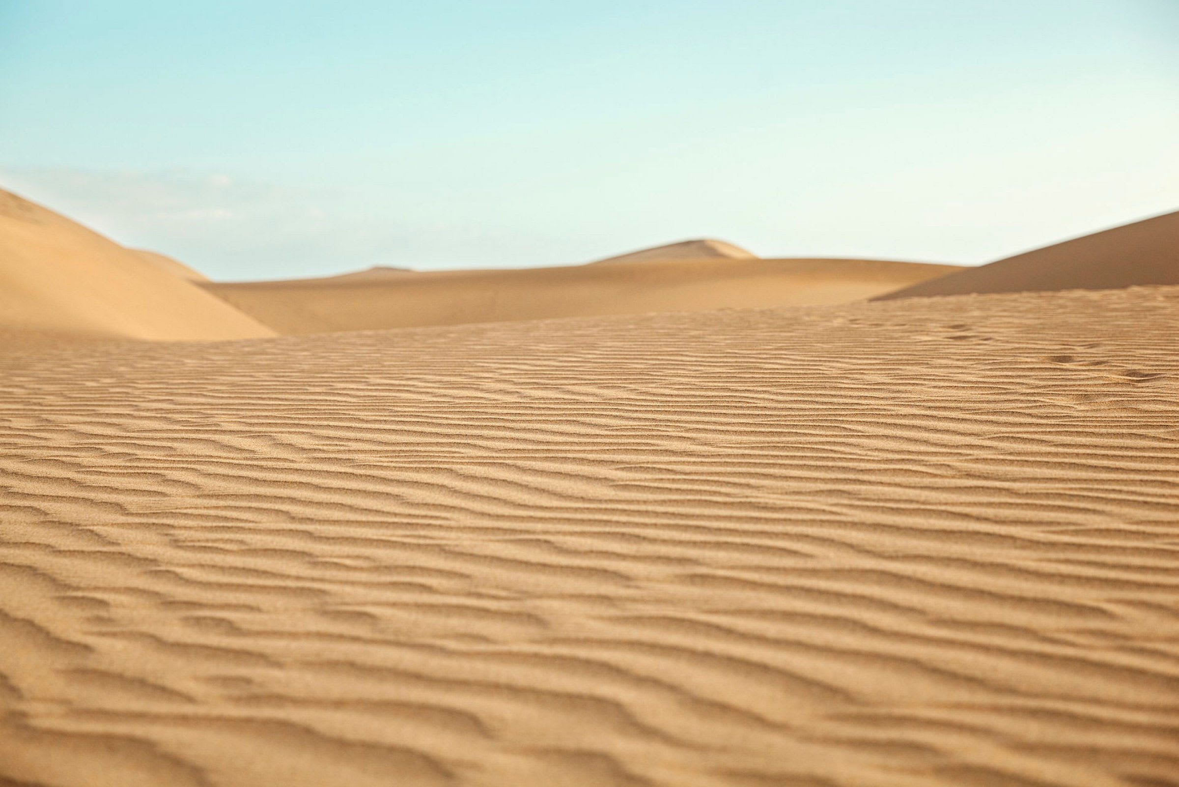 Bild av sanddyner med fint mönstrad sand. Klart blå himmel i bakgrunden. (AI-genererad text)