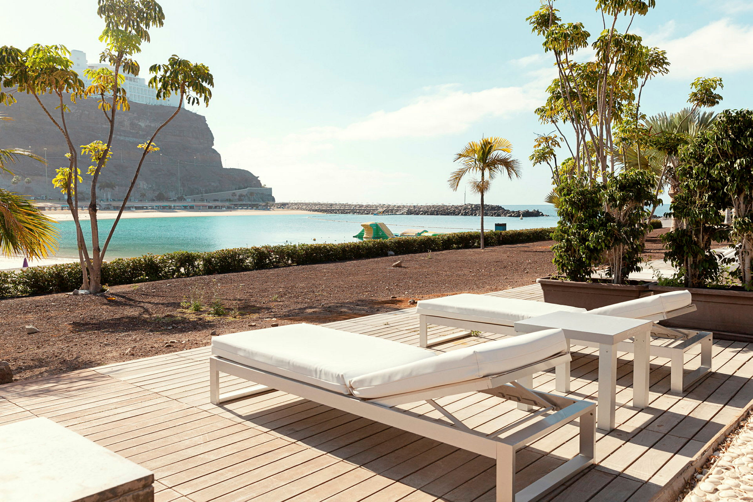 Solstolar på en terrass med utsikt över en strand och hav. (AI-genererad text)