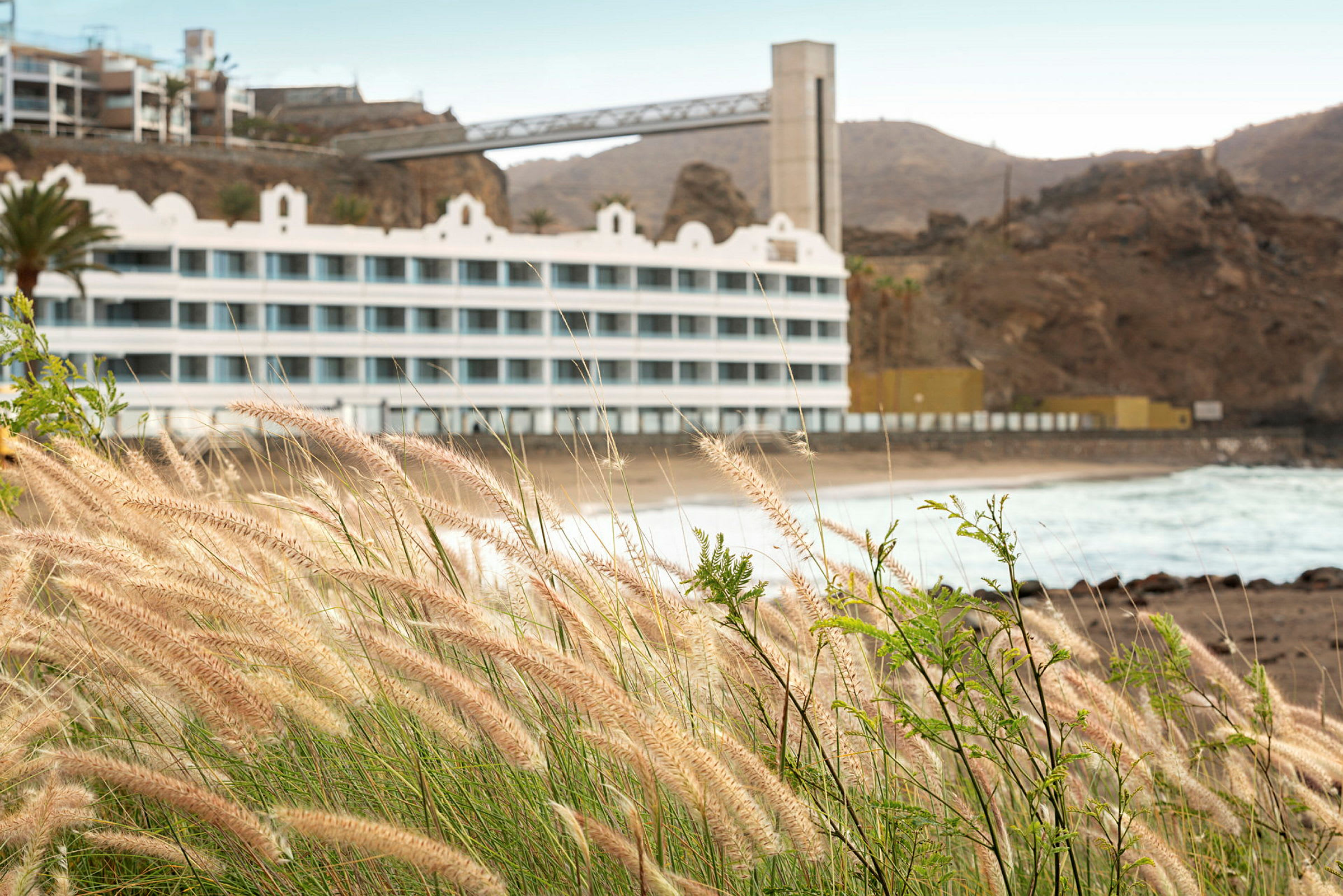 Bild av ett hotell vid en klippig strand med gräs i förgrunden. (AI-genererad text)