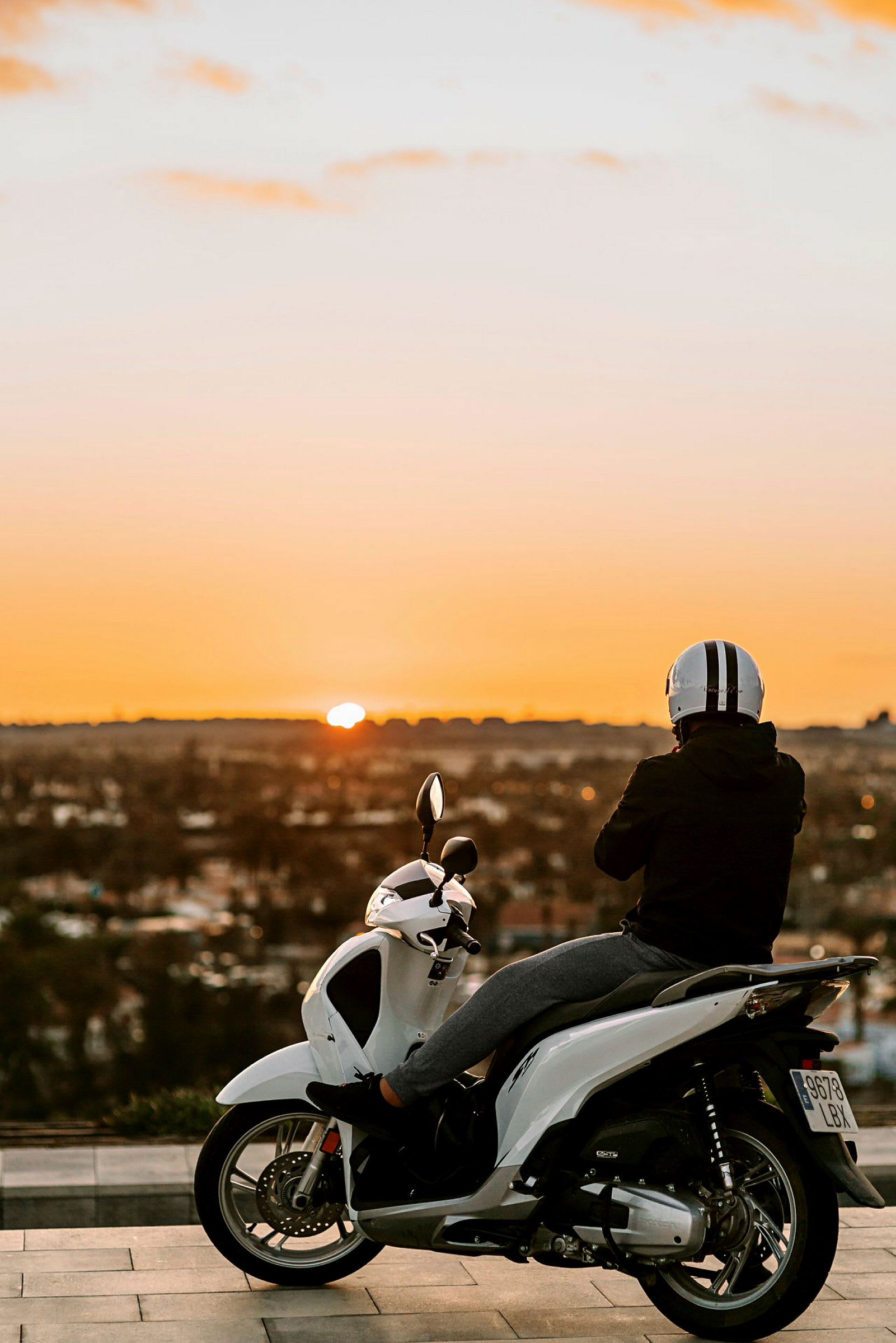En person sitter på en vit scooter och ser på solnedgången. (AI-genererad text)