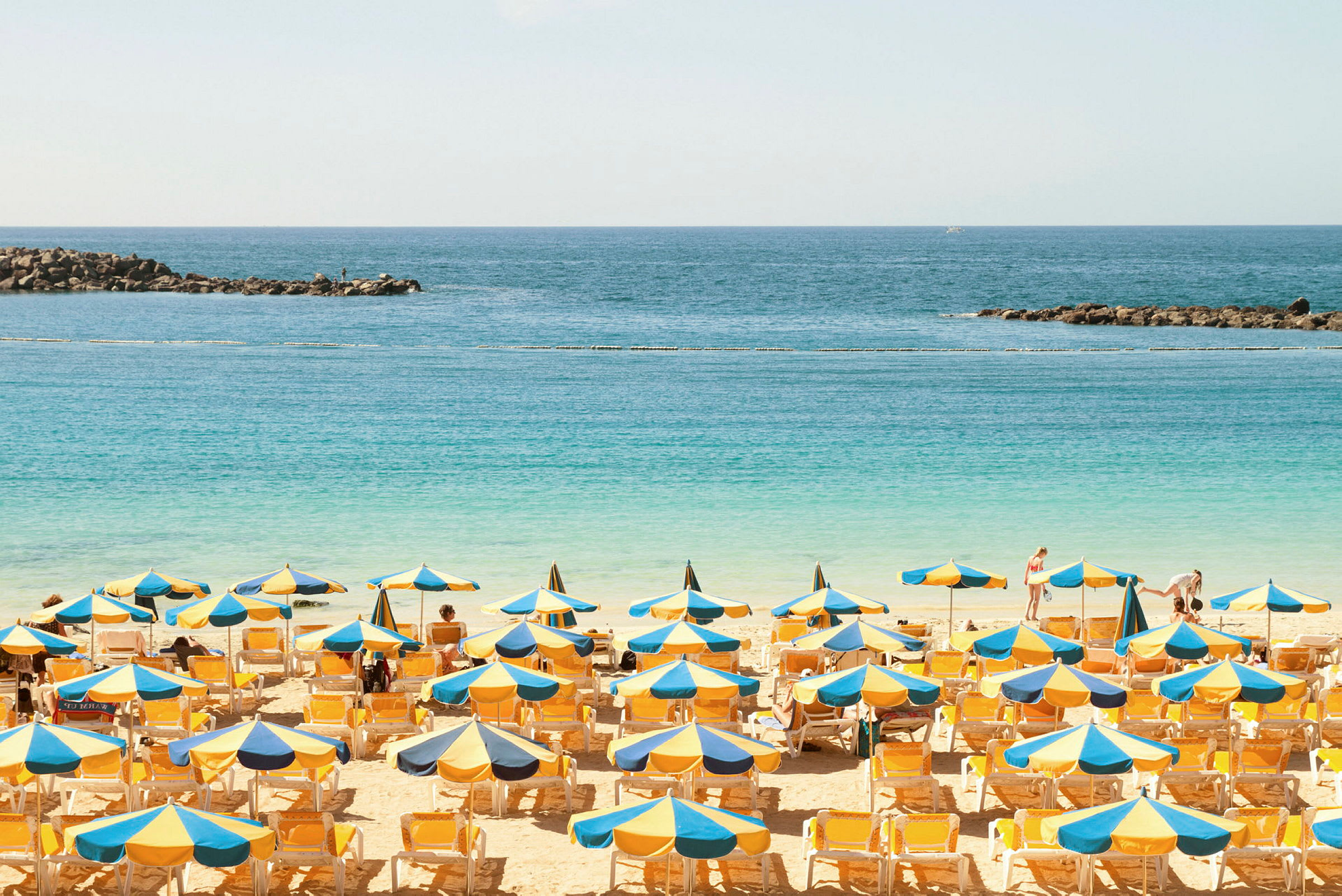 Strand med solstolar och parasoller framför havet. (AI-genererad text)