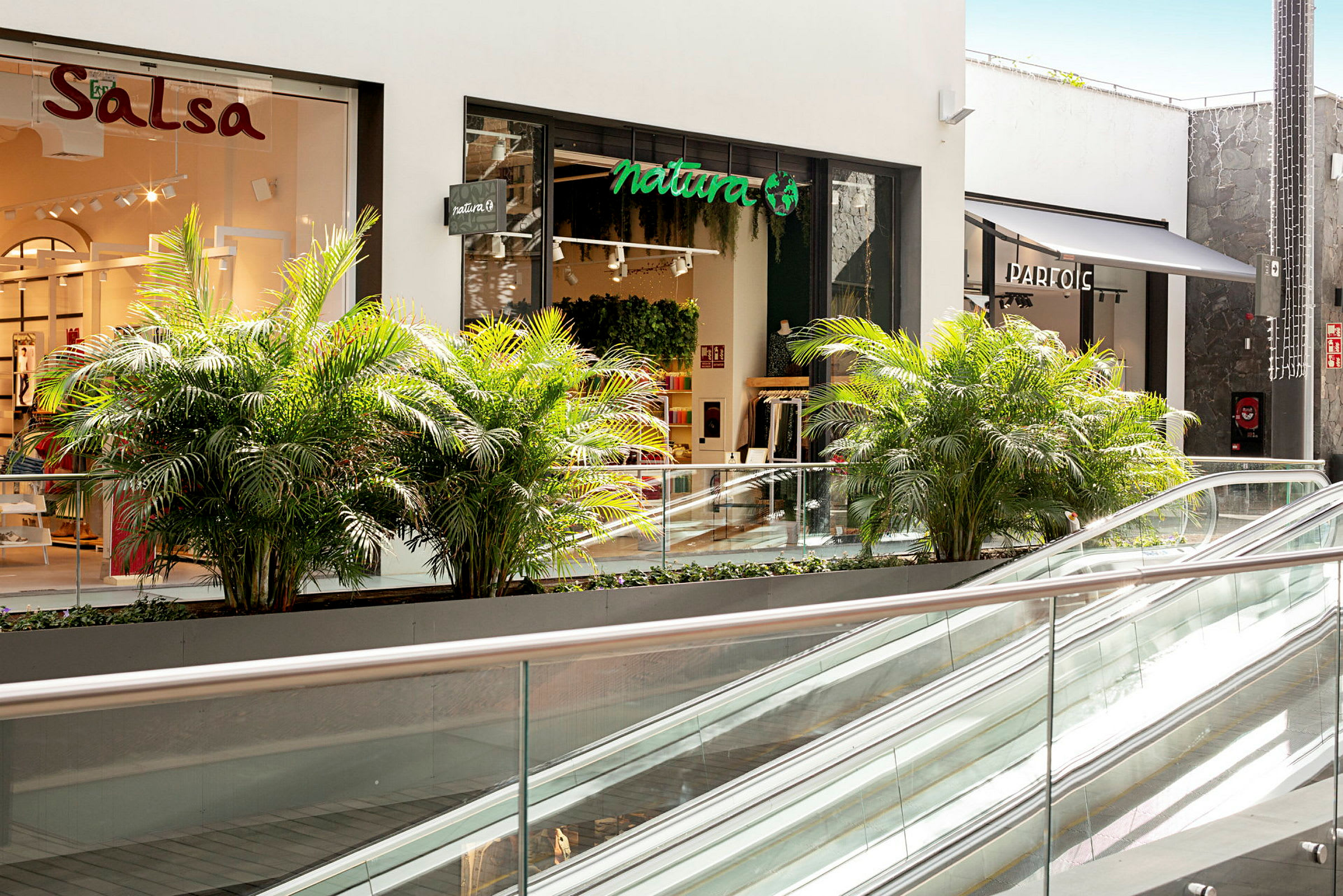 En shoppinggalleria med butiker, växter och rulltrappor. (AI-genererad text)