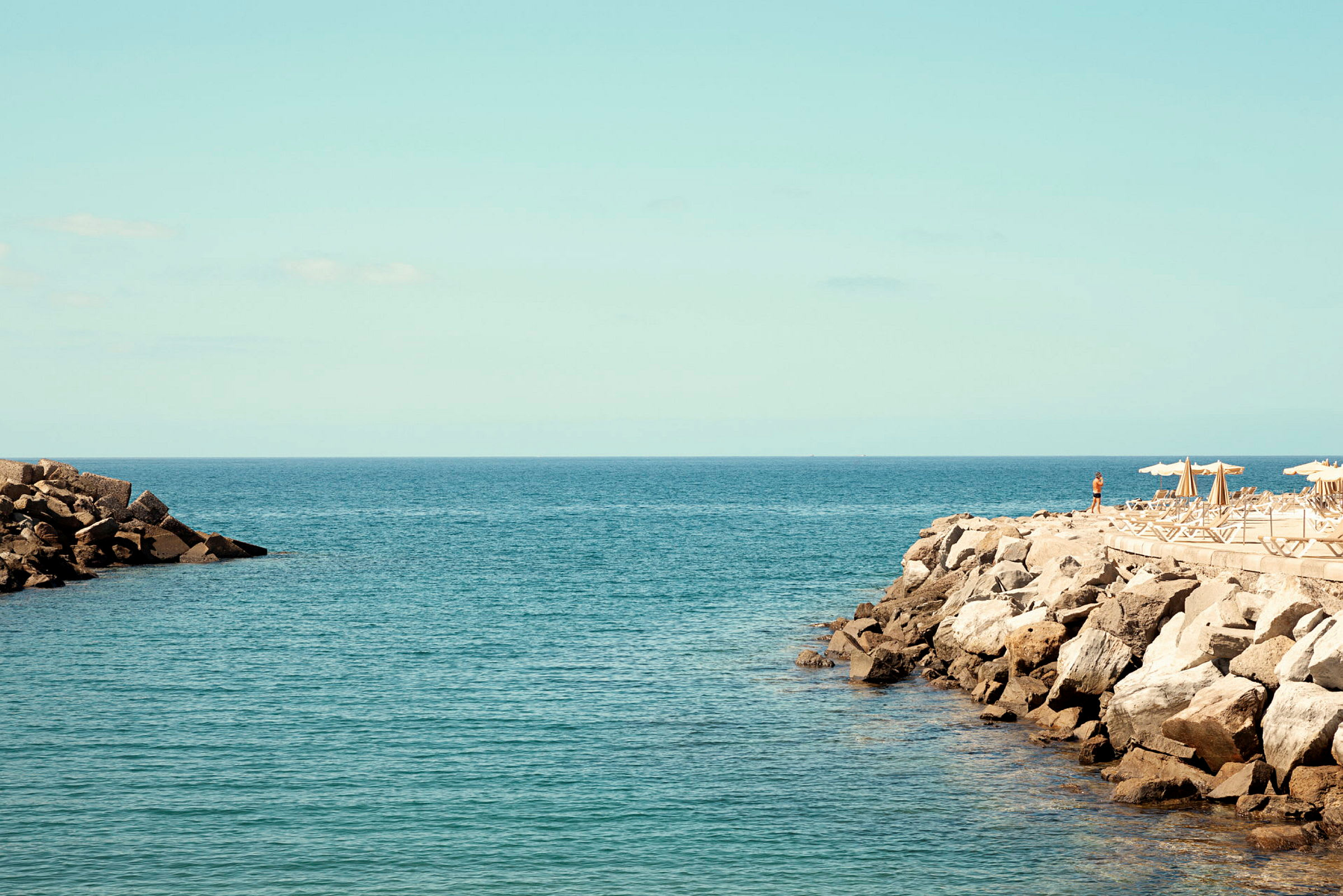 Vy över havet med stenig kust och solstolar under parasoller. (AI-genererad text)