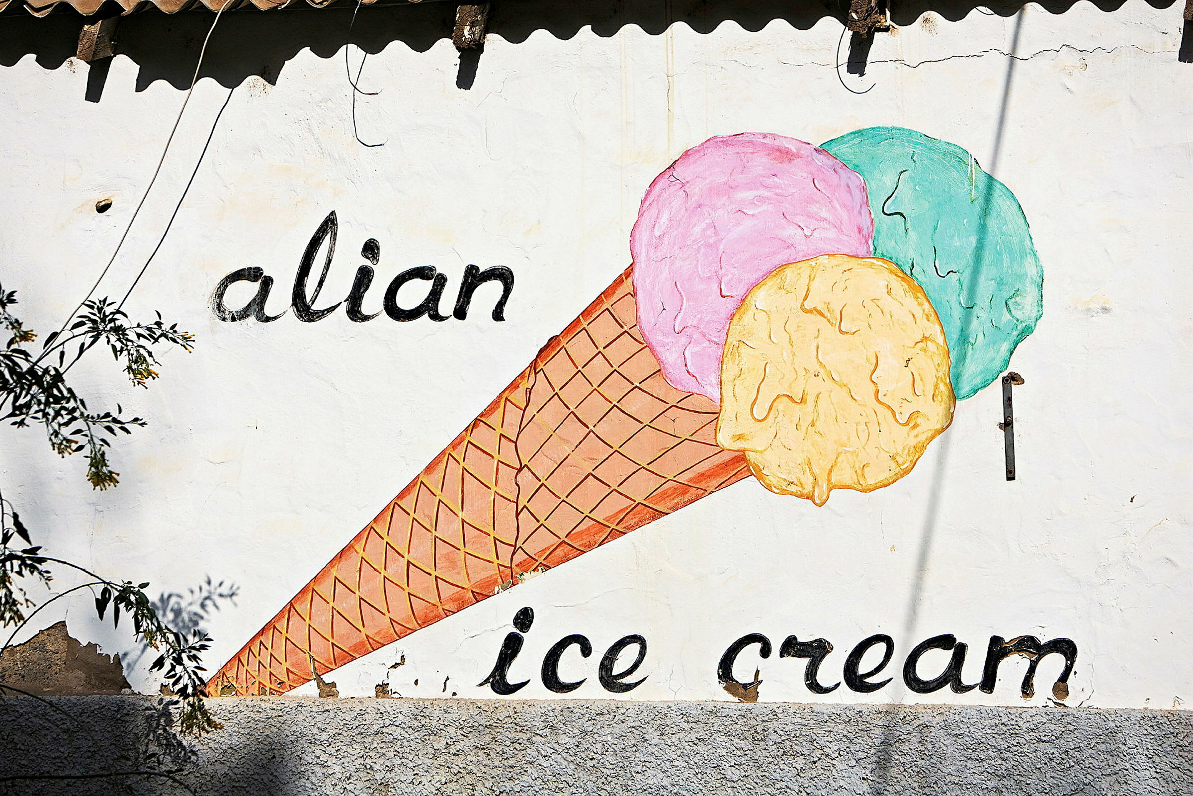 Målning av en glasstrut med tre färgglada kulor på en vägg med texten 'alian ice cream'. (AI-genererad text)