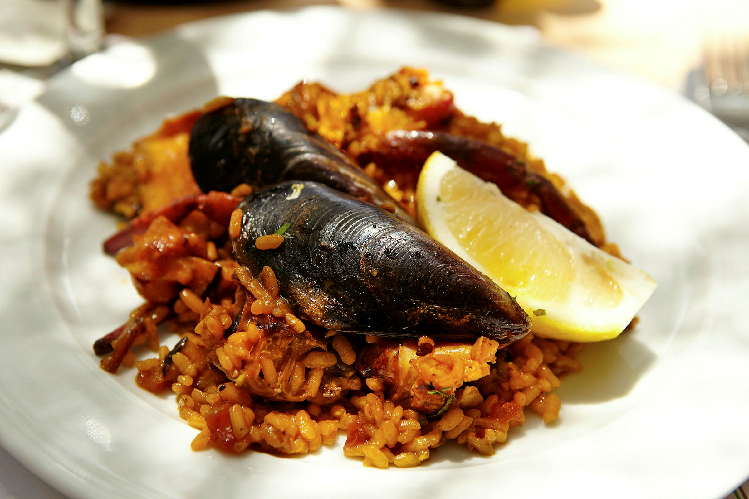En tallrik med paella innehållande musslor, kryddat ris och en citronklyfta. (AI-genererad text)