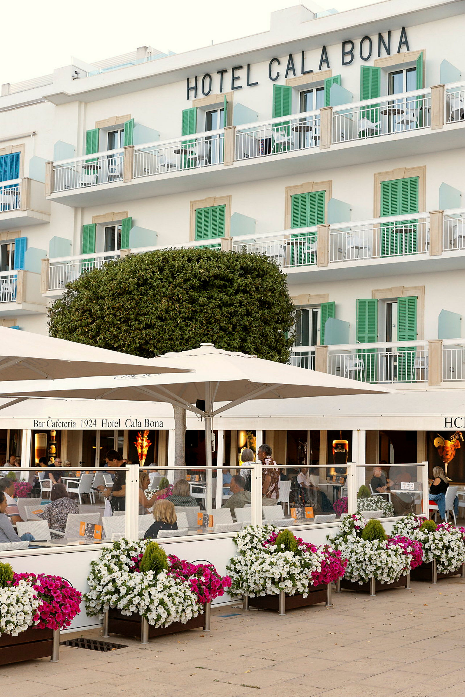 Hotellbyggnad med balkonger, utomhuscafé med färgglada blomsterlådor i förgrunden. (AI-genererad text)