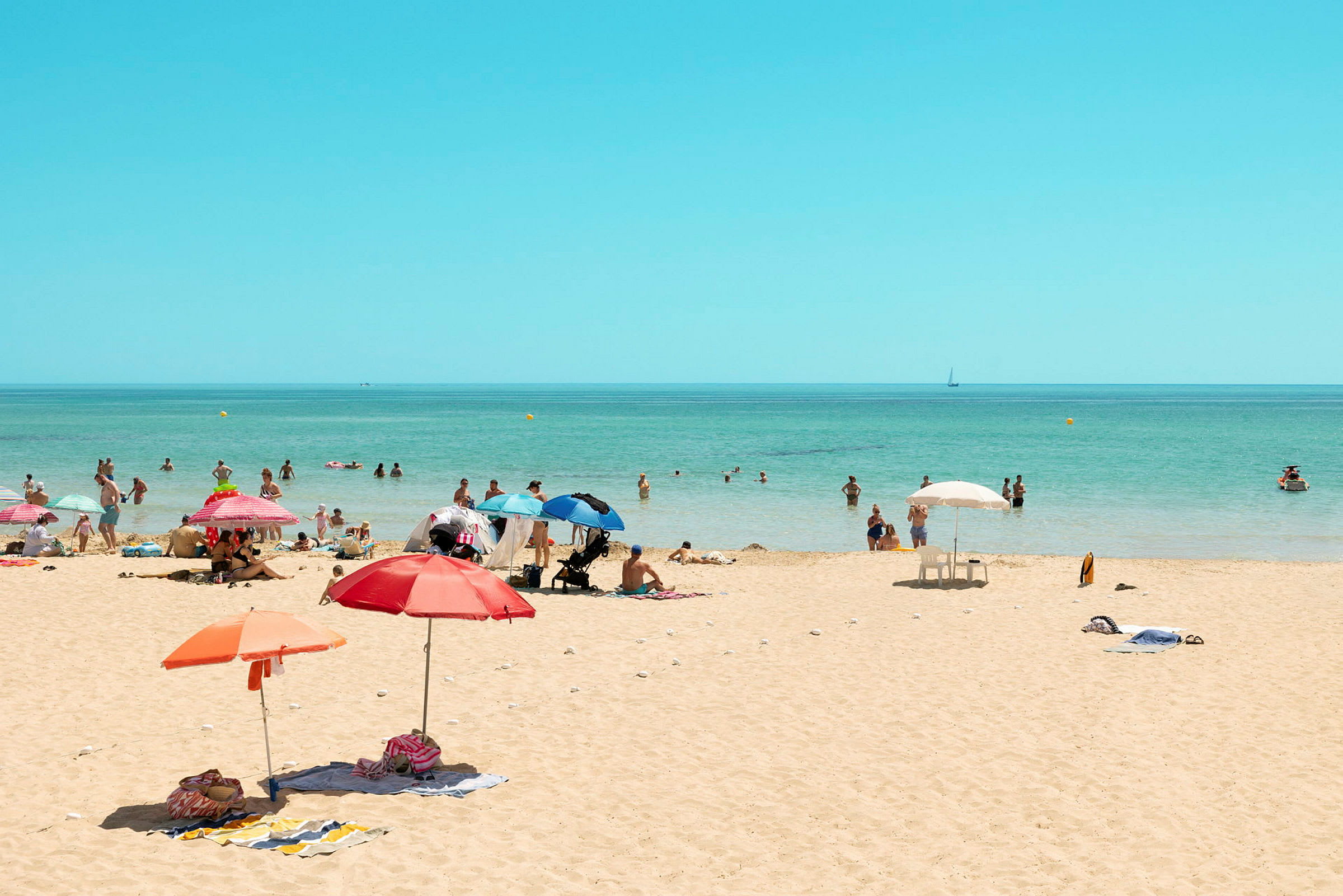 En sandstrand med parasoller och människor som njuter av vattnet. (AI-genererad text)