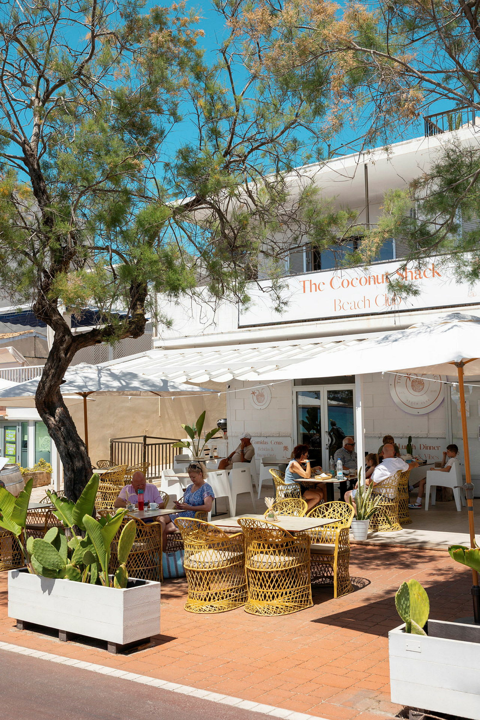 Ett café med uteservering under ett träd och parasollar. (AI-genererad text)