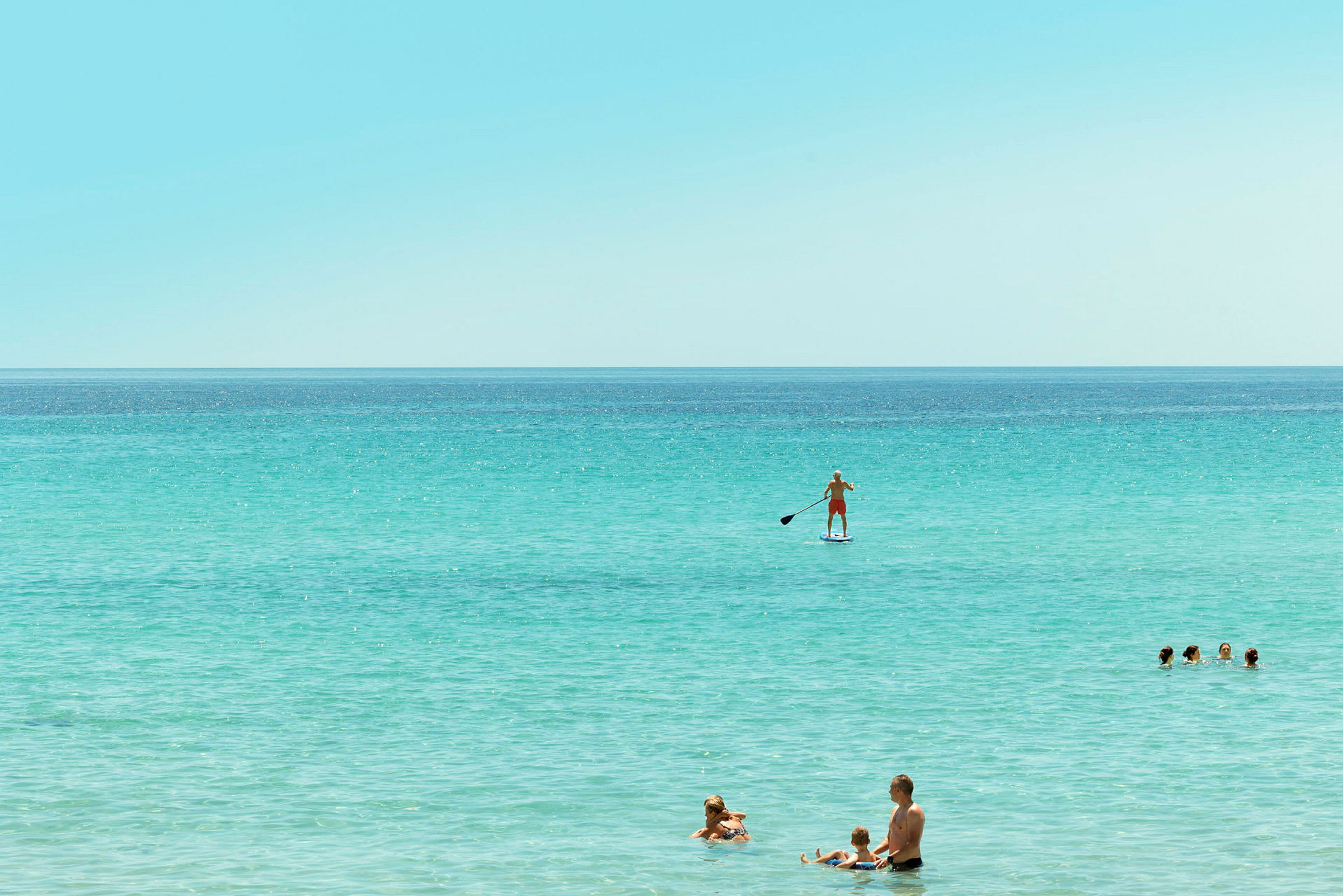 Personer i vattnet med en som paddlar på en paddleboard. (AI-genererad text)