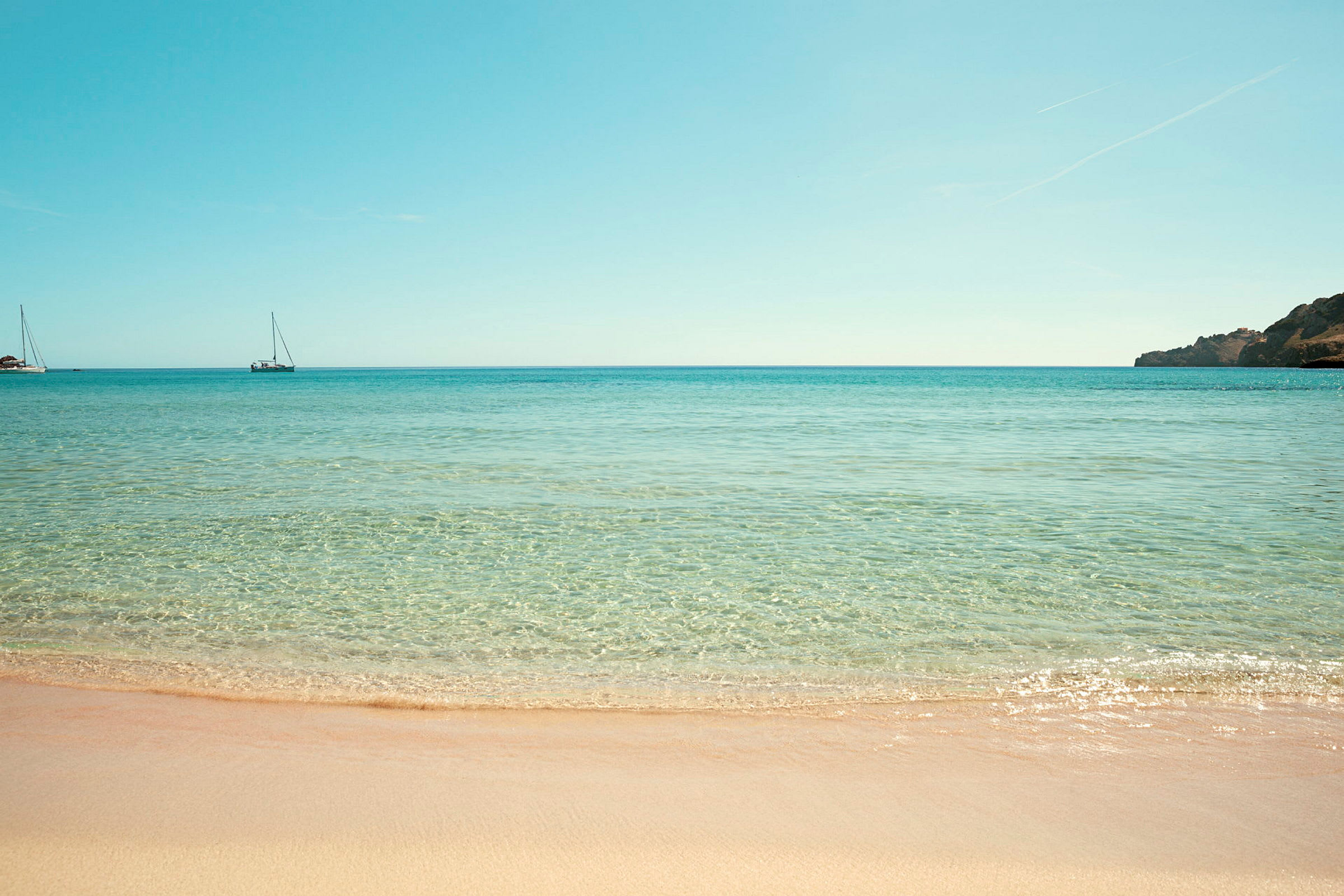 Strand med klart vatten och två segelbåtar i havet. (AI-genererad text)
