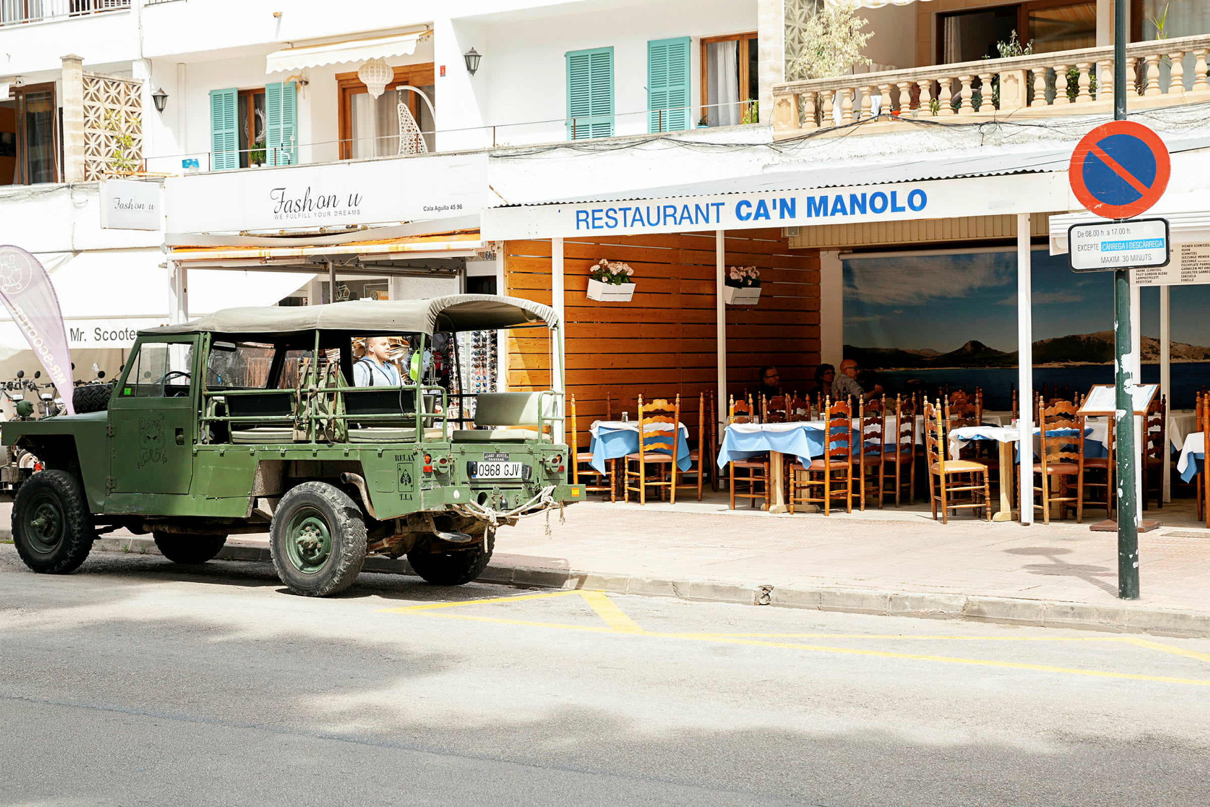 En grön militär jeep parkerad framför restaurangen Can Manolo. (AI-genererad text)