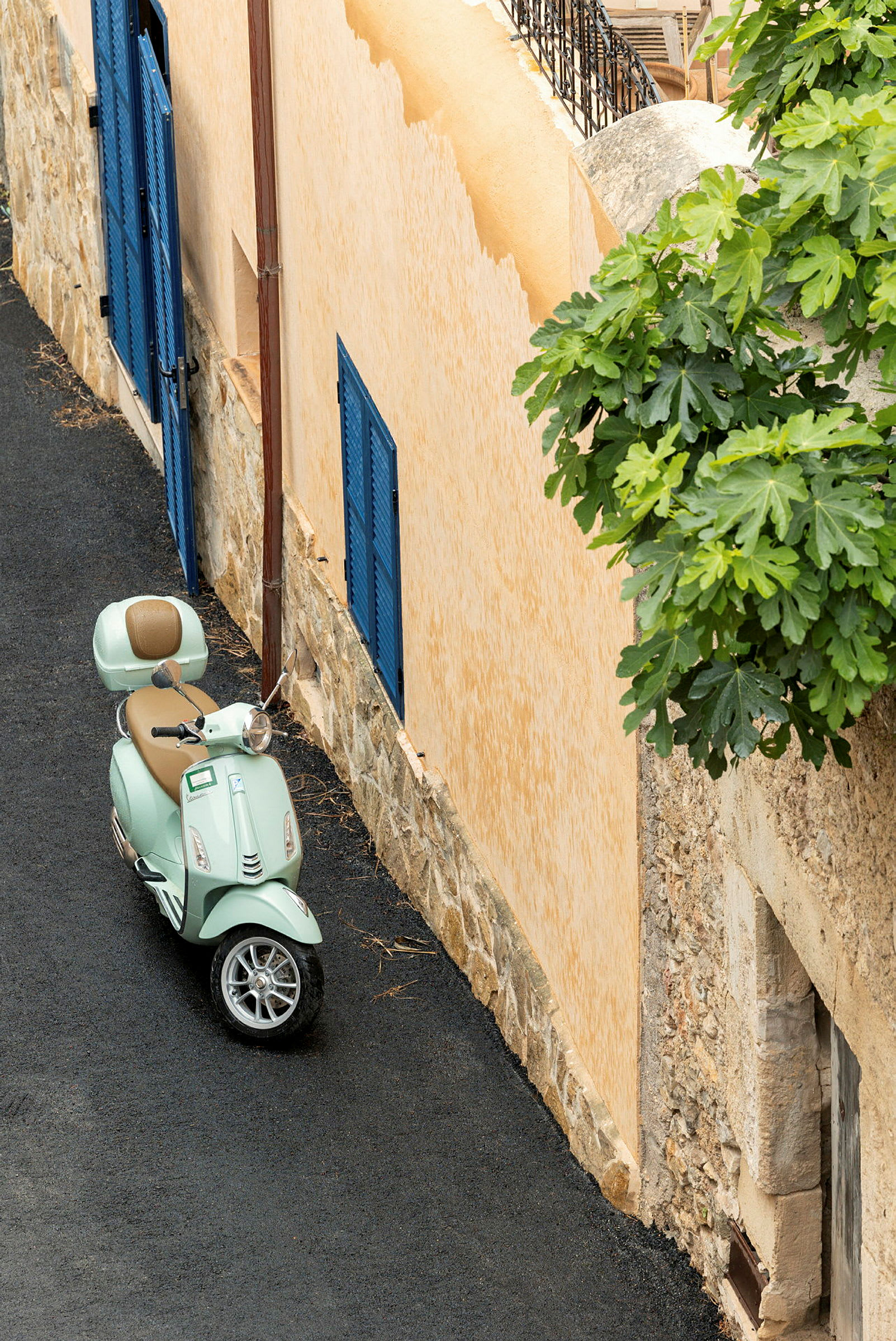 En ljusgrön scooter står parkerad vid en beige byggnad med blåa träfönsterluckor. (AI-genererad text)