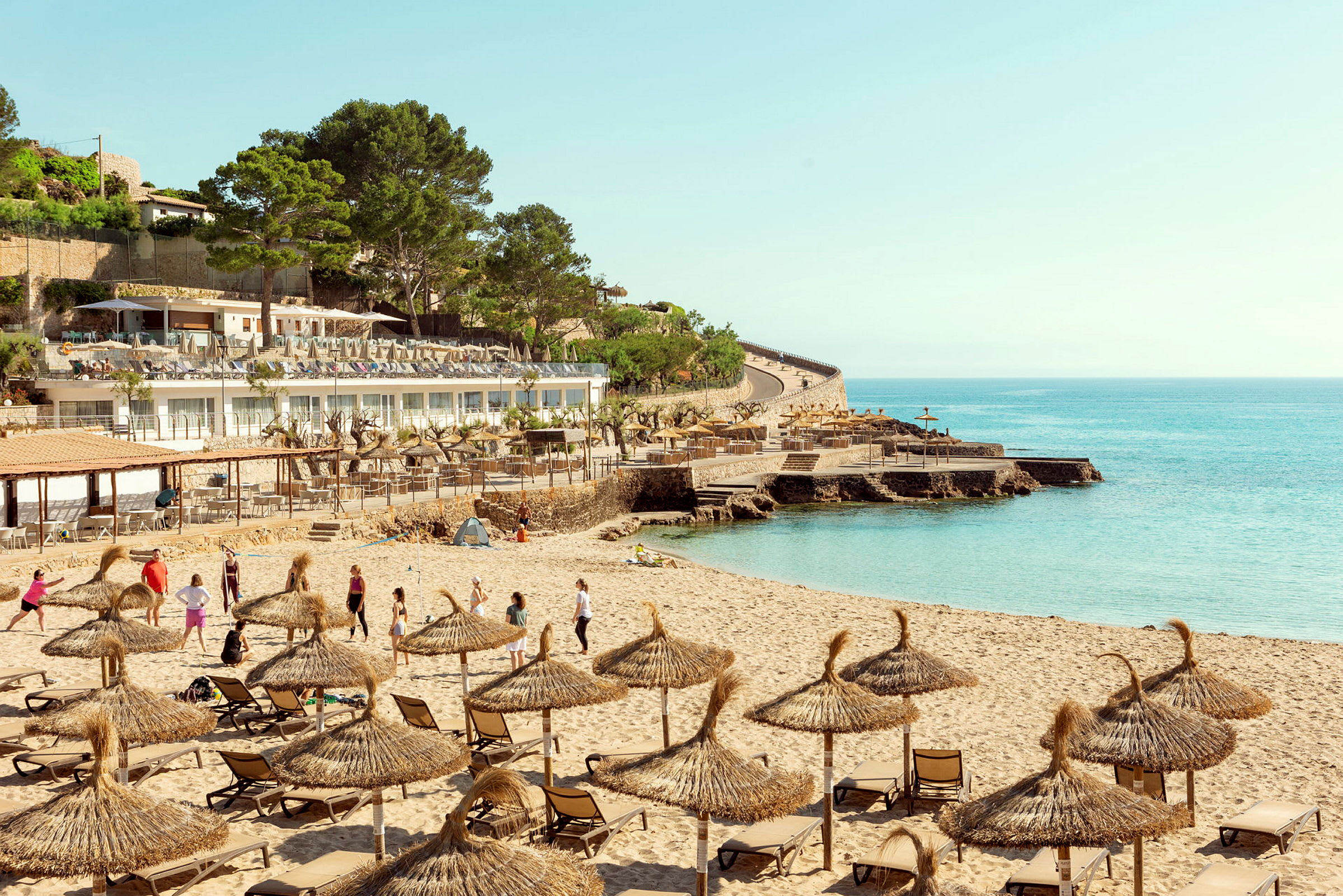 Strand med parasoller och solstolar, omgiven av byggnader och hav. (AI-genererad text)