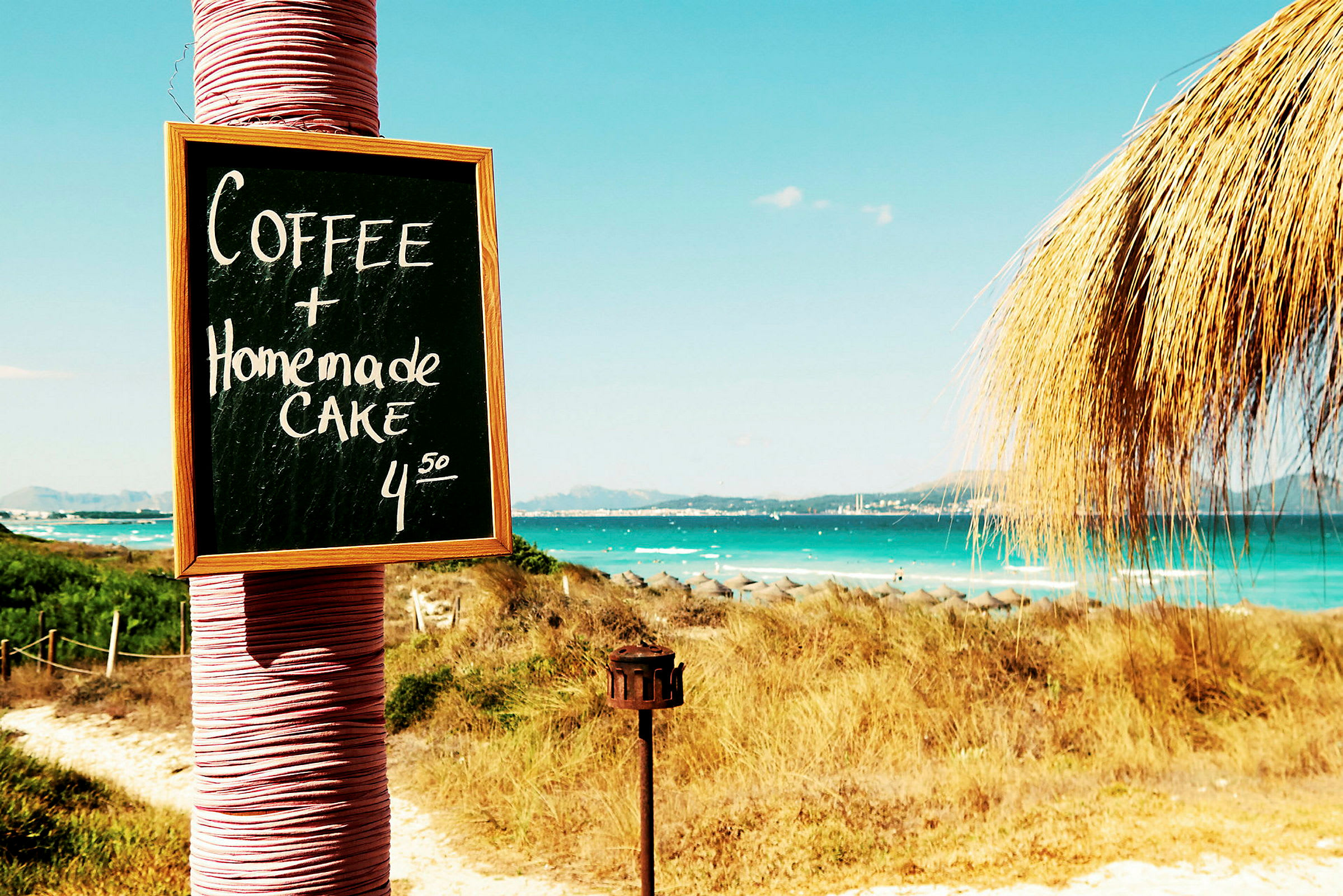 Skylt med texten 'Coffee + Homemade Cake 4.50' vid stranden. (AI-genererad text)