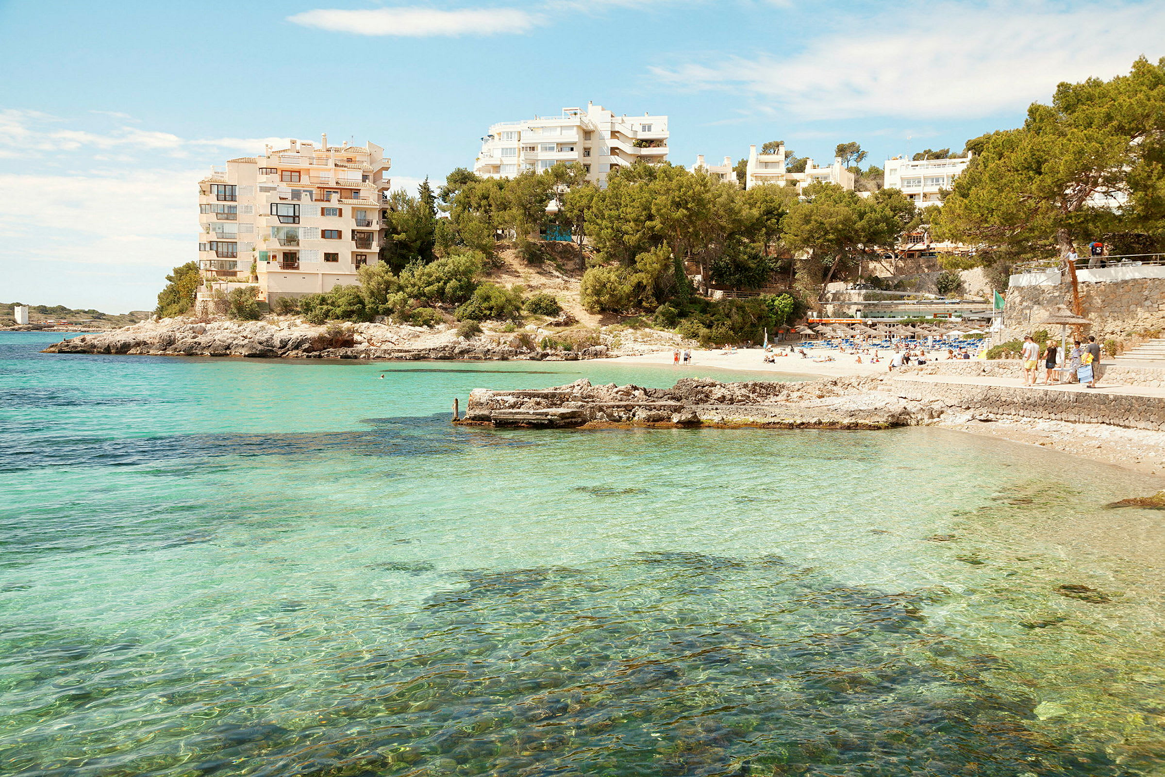 Bild av en kustlinje med klart blått vatten, en strand och omgivande byggnader. (AI-genererad text)