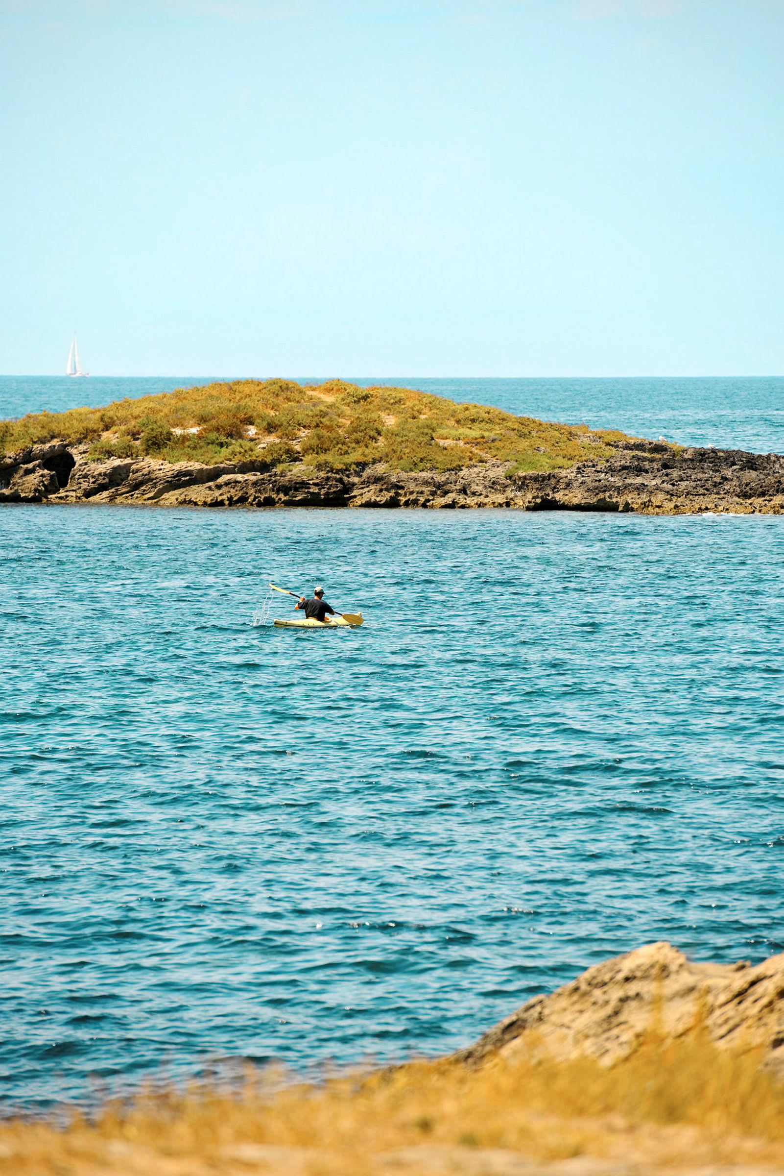 En person paddlar kajak på havet nära en liten grön ö. (AI-genererad text)
