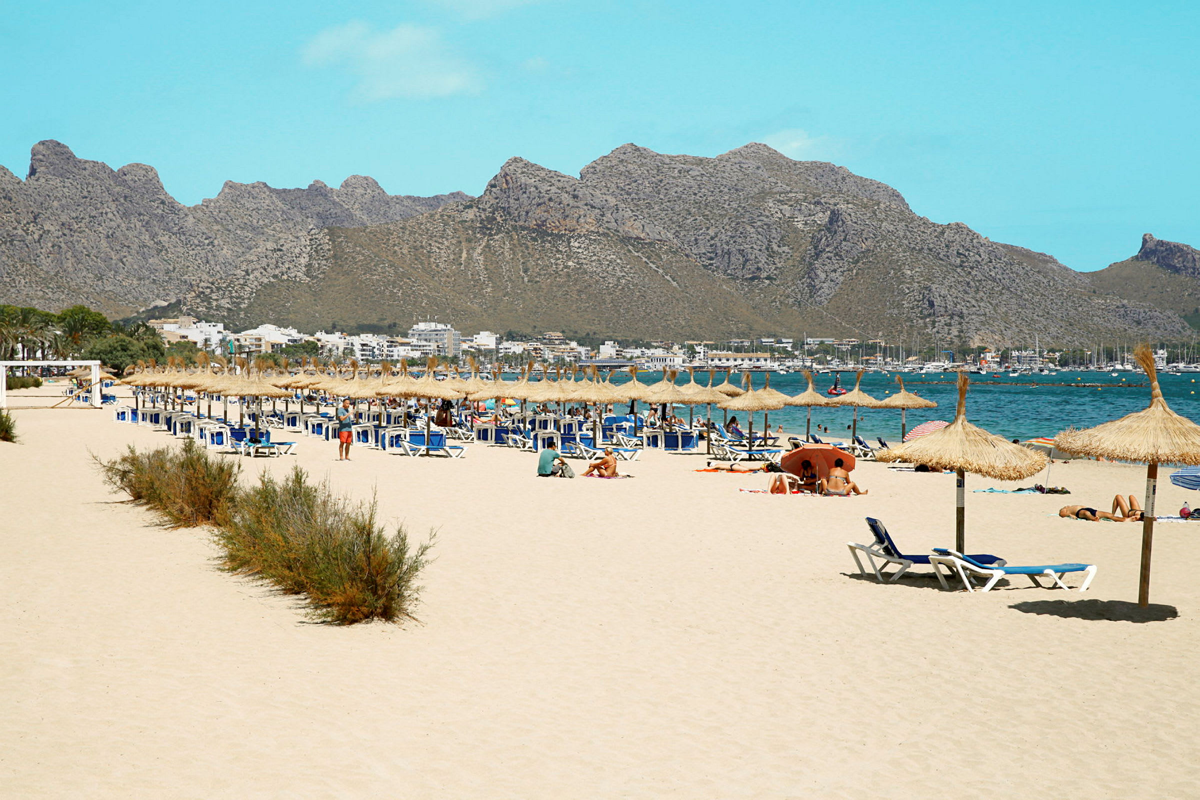 Sandstrand med solstolar och parasoller, omgiven av berg. (AI-genererad text)