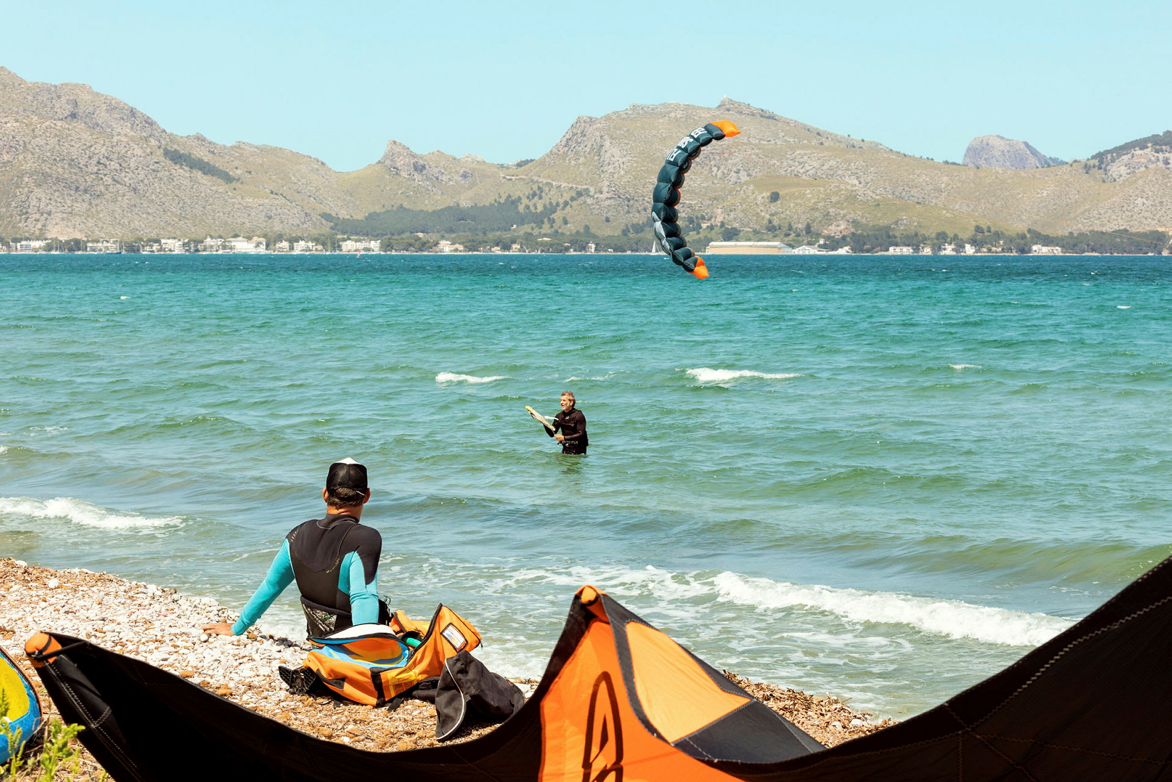 Person som kitesurfar nära strandkant, med berg i bakgrunden. (AI-genererad text)