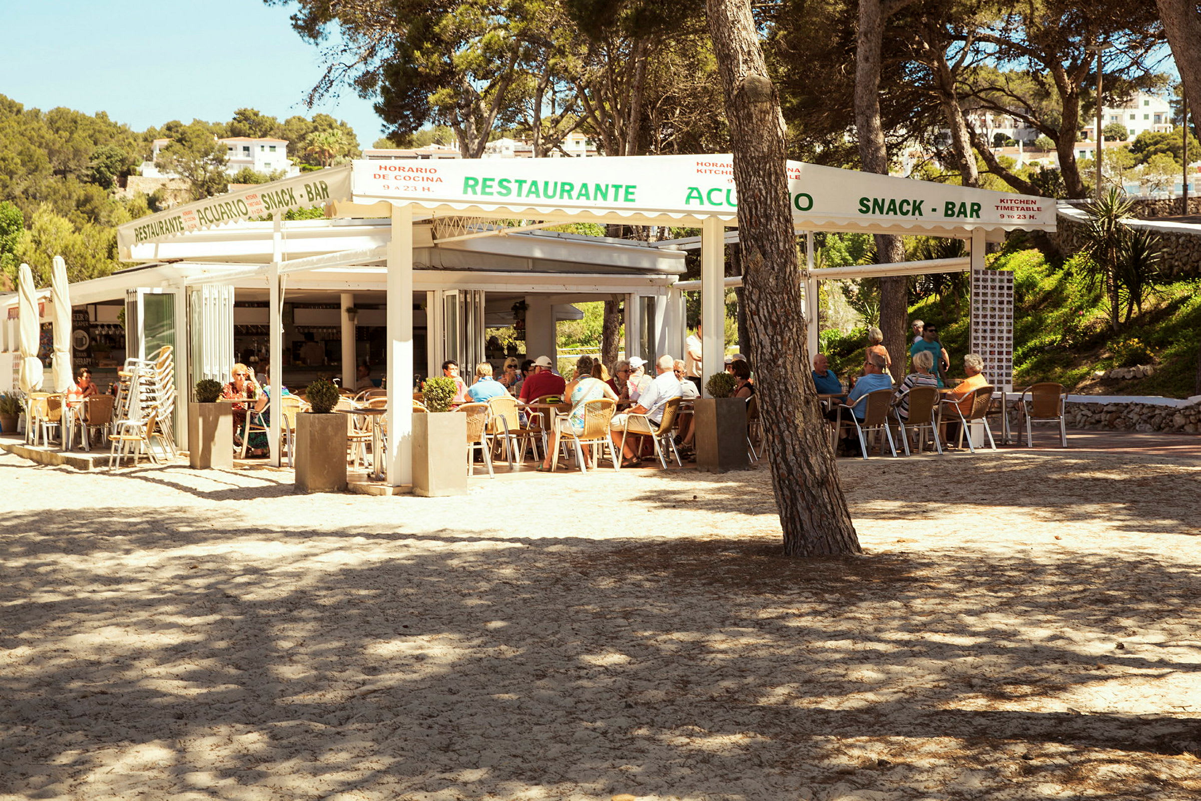 En utomhusrestaurang med gäster som sitter vid bord under ett tak. (AI-genererad text)