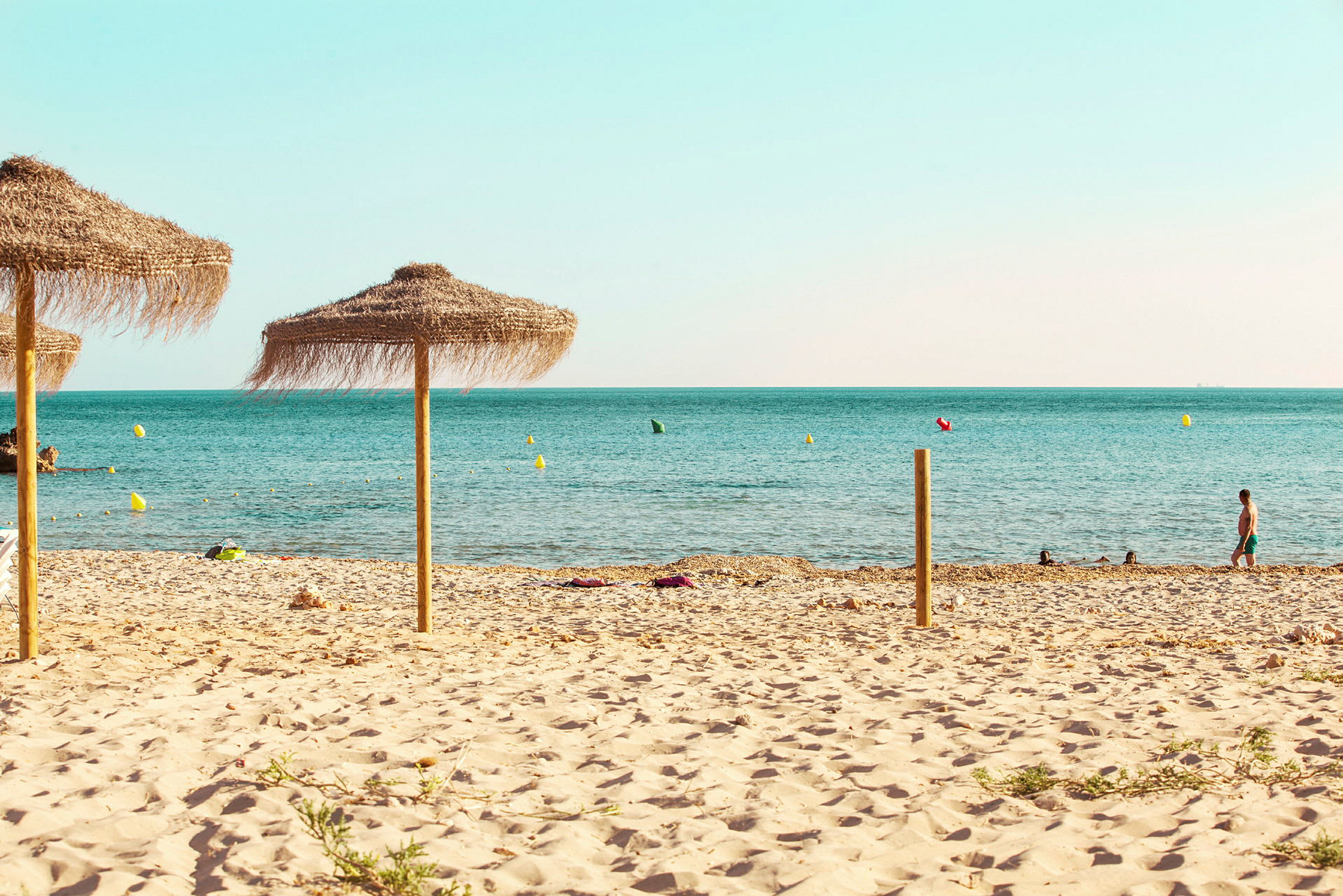 En sandstrand med parasoller i förgrunden och havet i bakgrunden. (AI-genererad text)
