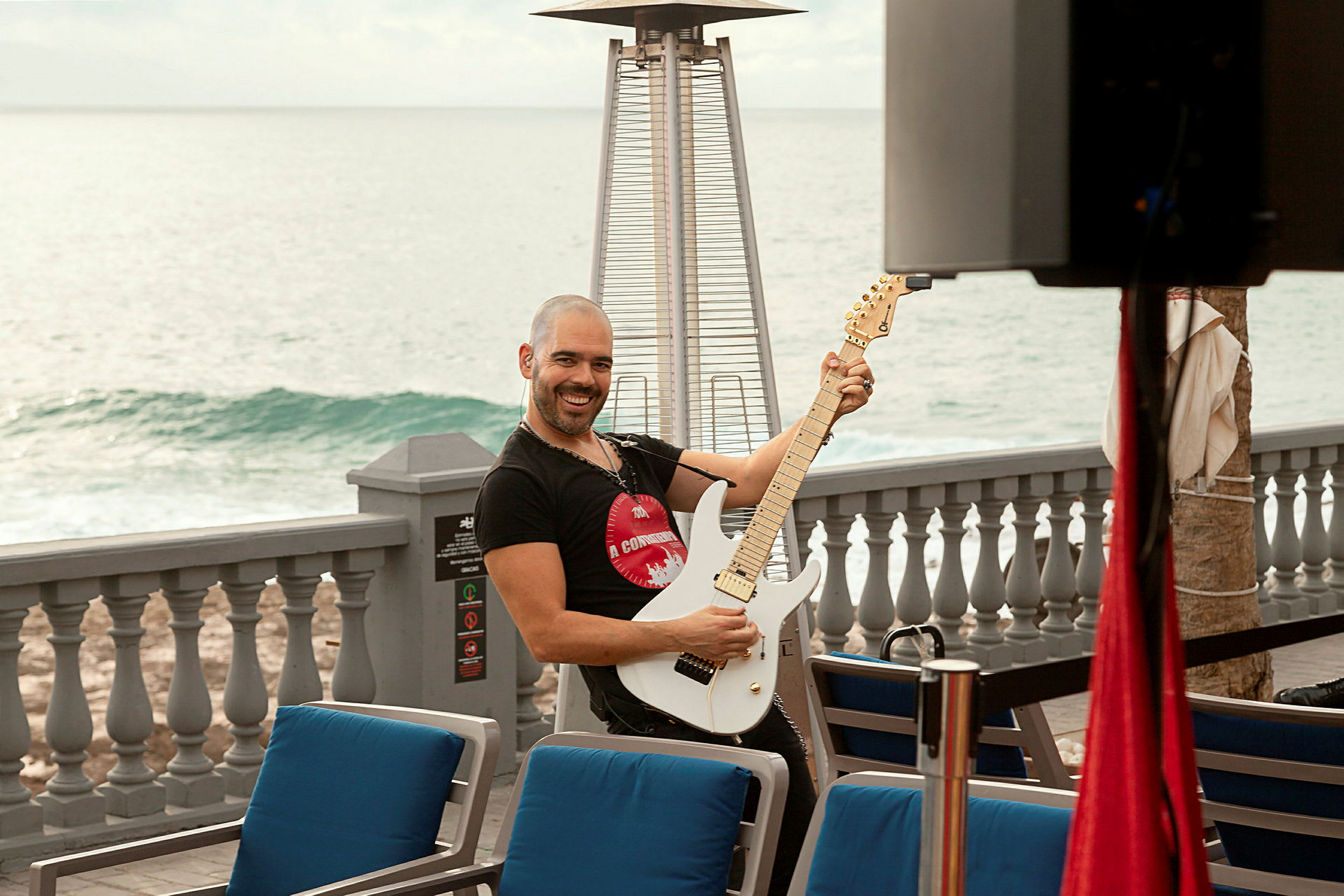 Person spelar elgitarr vid uteservering med havet i bakgrunden. (AI-genererad text)
