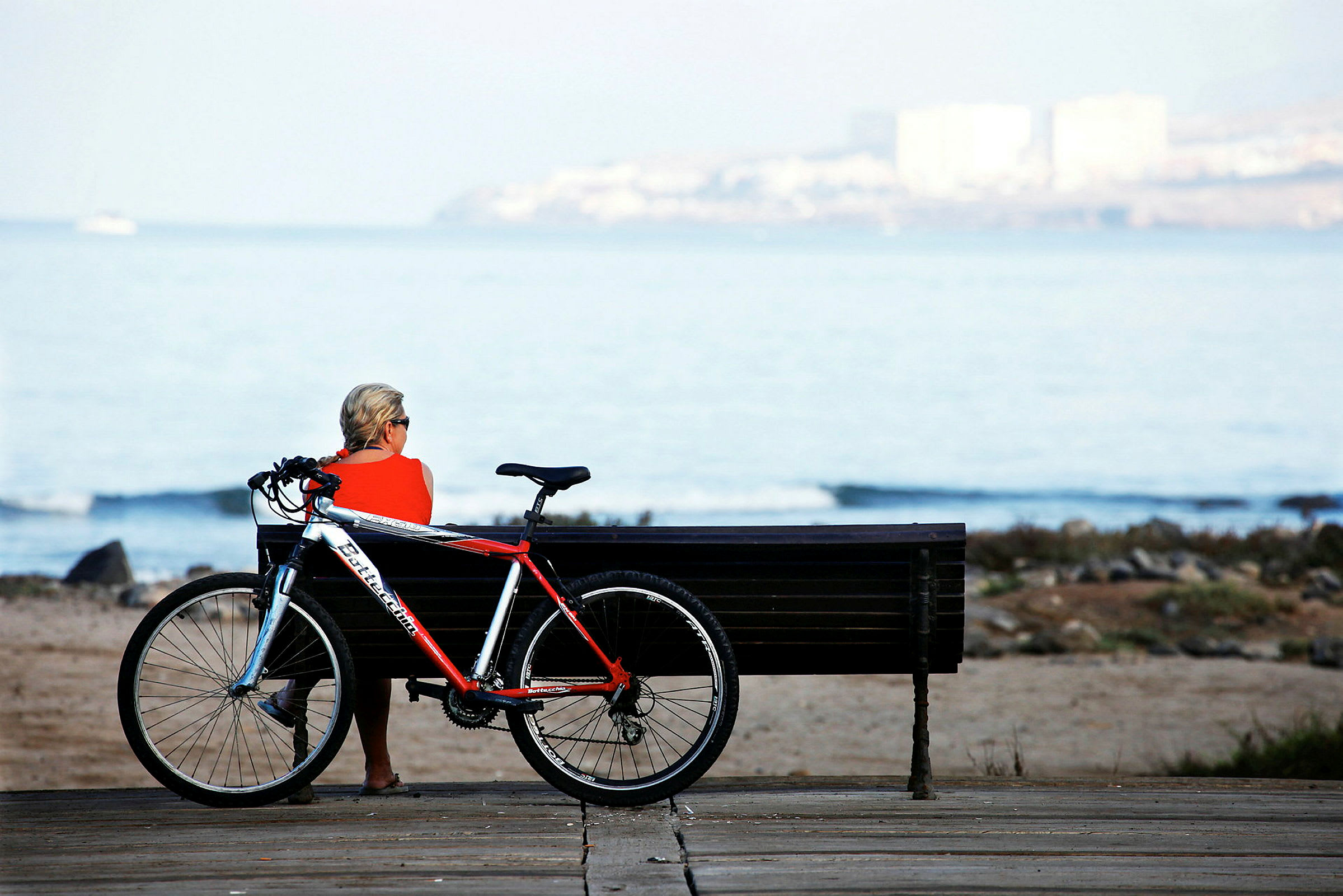 En person sitter på en bänk vid stranden med en cykel vid sidan. (AI-genererad text)
