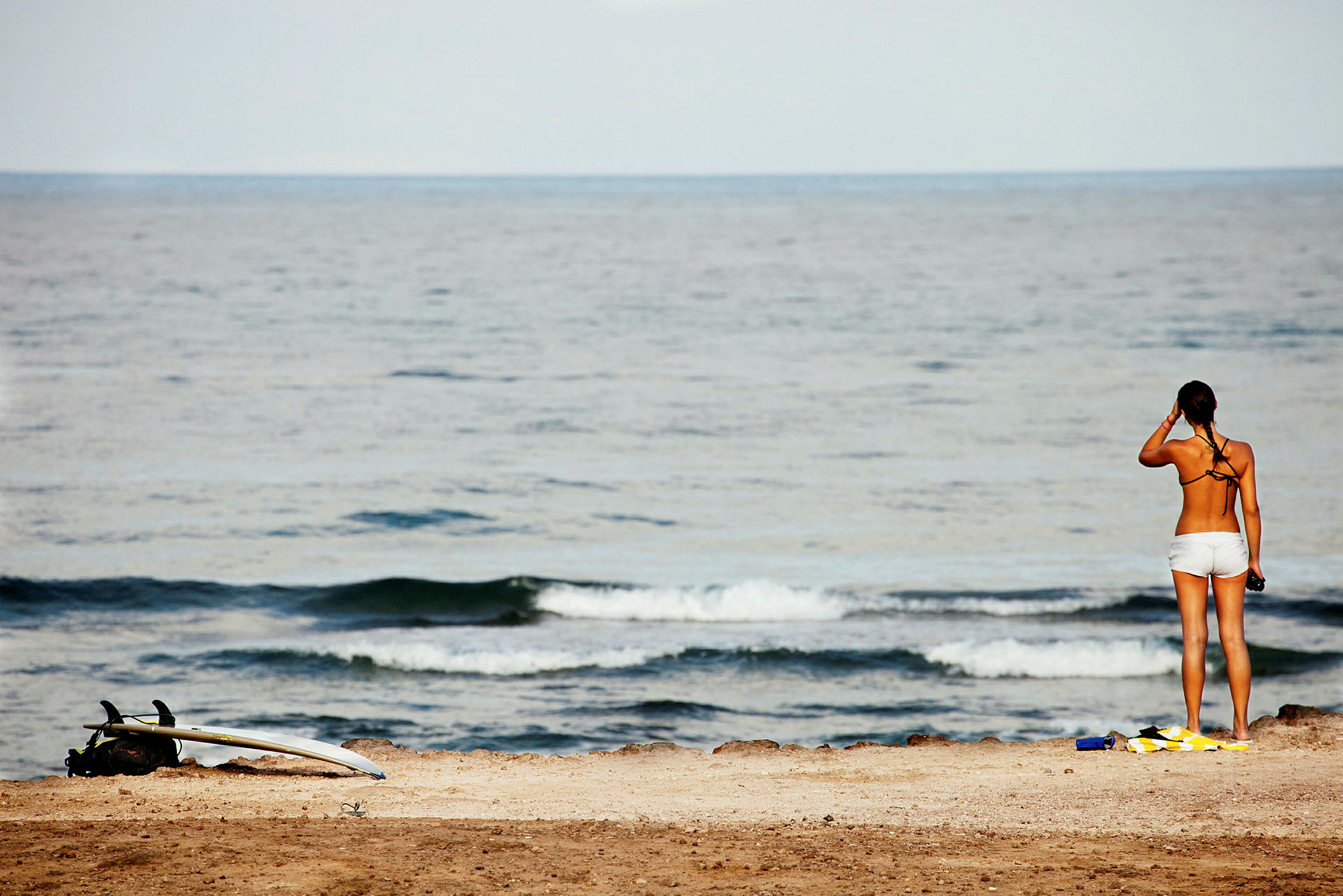 En kvinna står på en strand och tittar ut över havet nära en surfbräda. (AI-genererad text)
