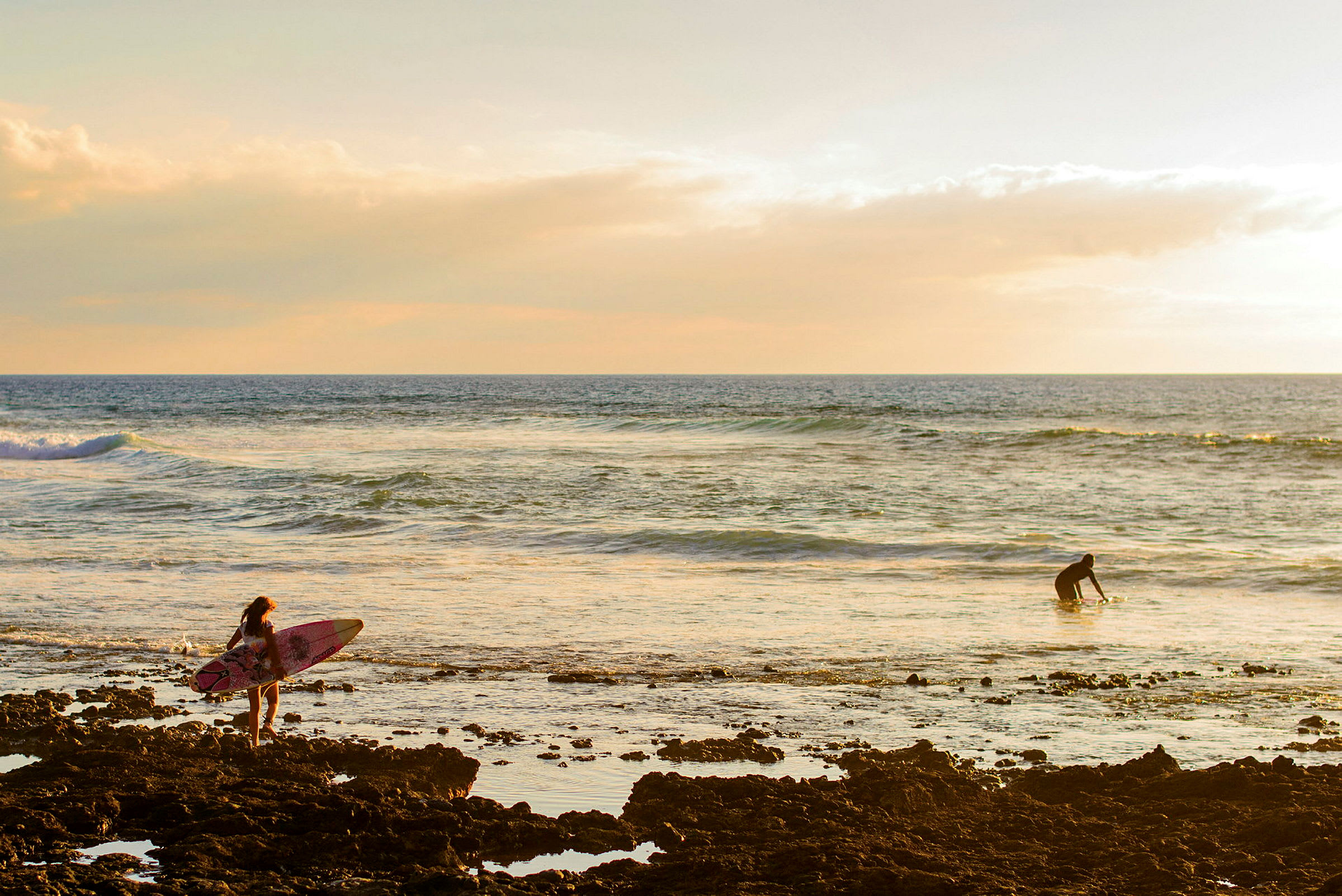 Två personer vid havet, en med surfbräda och den andre närmar sig vattnet. (AI-genererad text)