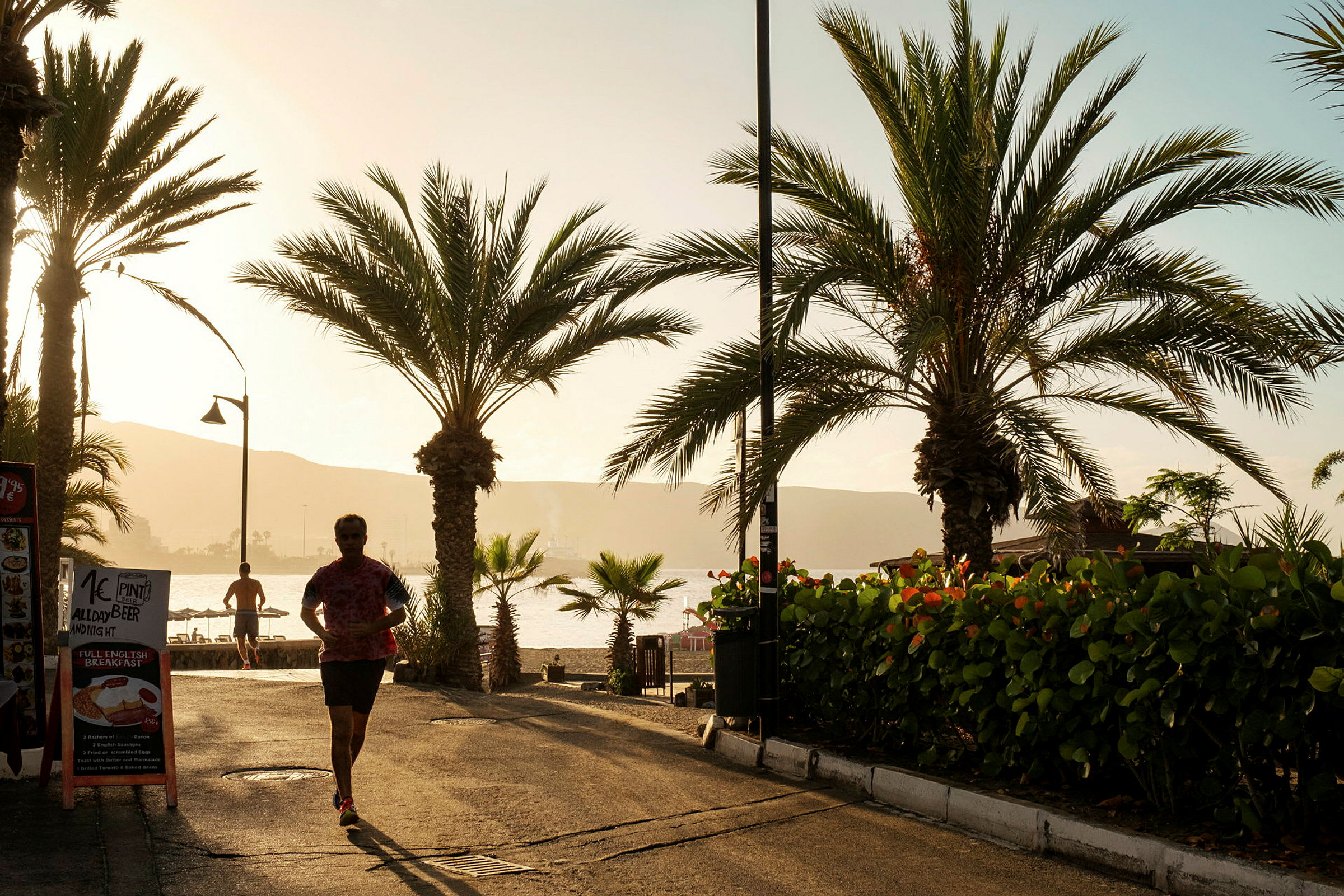 Gata med palmer och reklam för restauranger med solen i bakgrunden. (AI-genererad text)