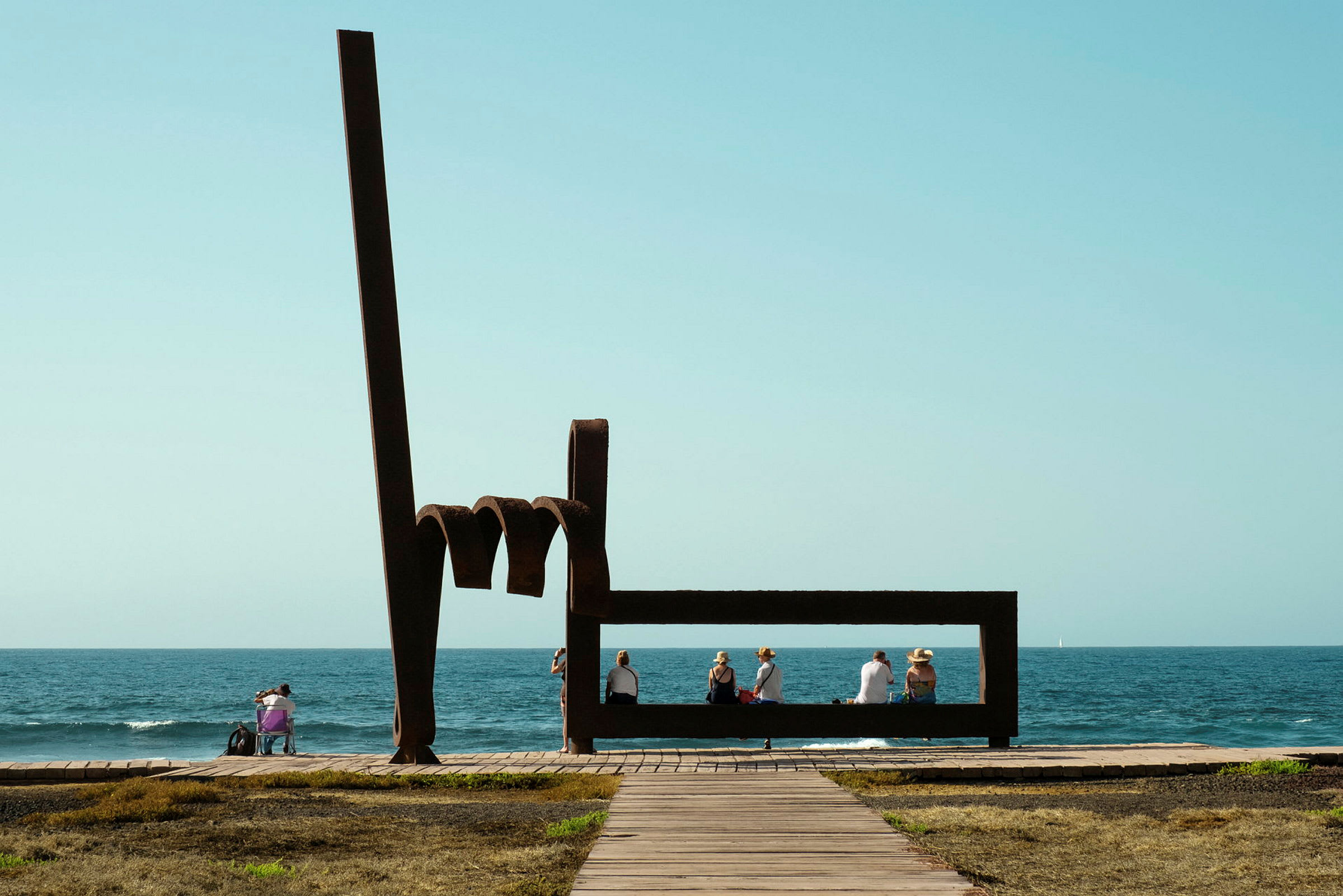 Skulptur med människor sittande vid havet. (AI-genererad text)