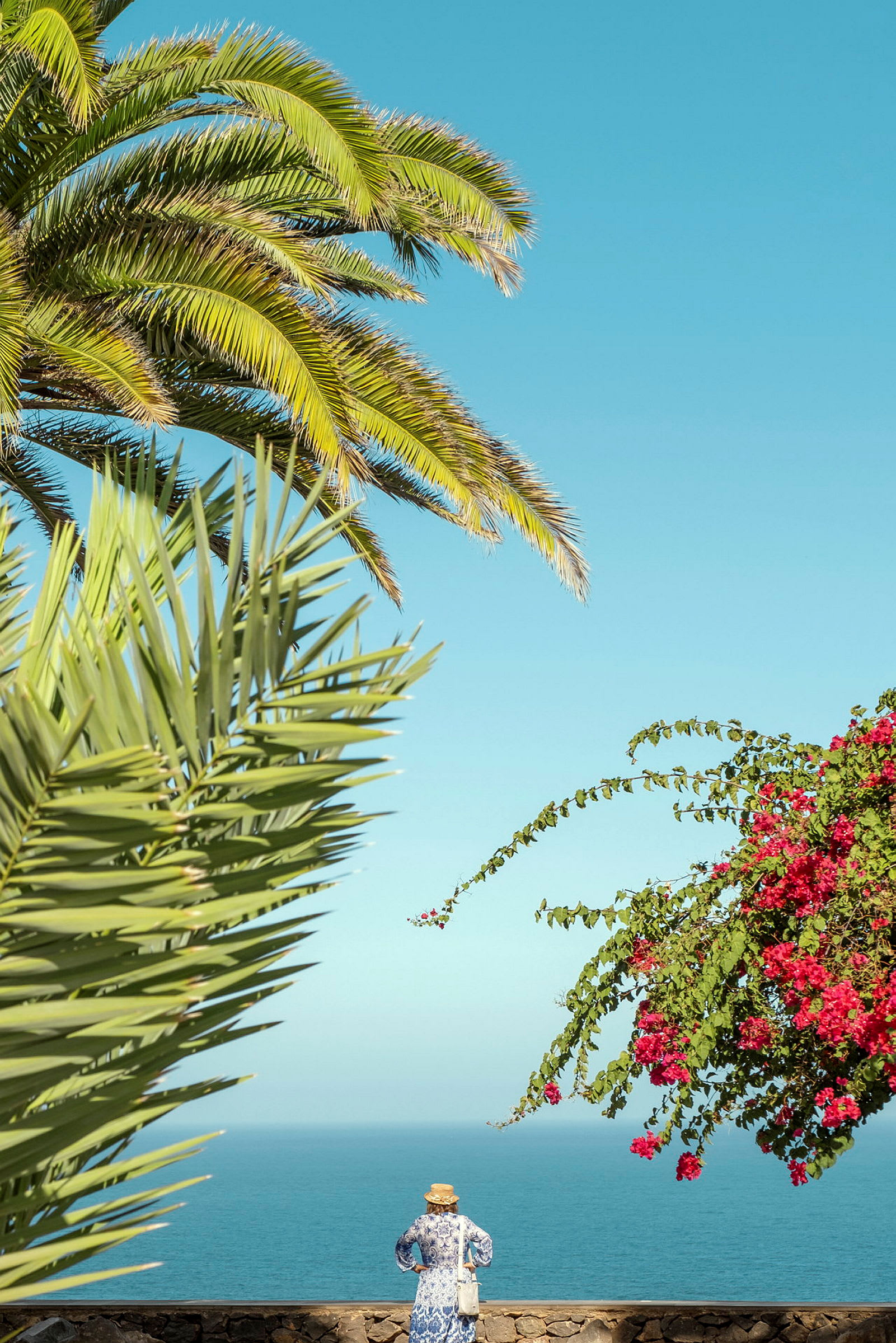 En kvinna står framför havet omgivet av palmer och blommande buskar. (AI-genererad text)