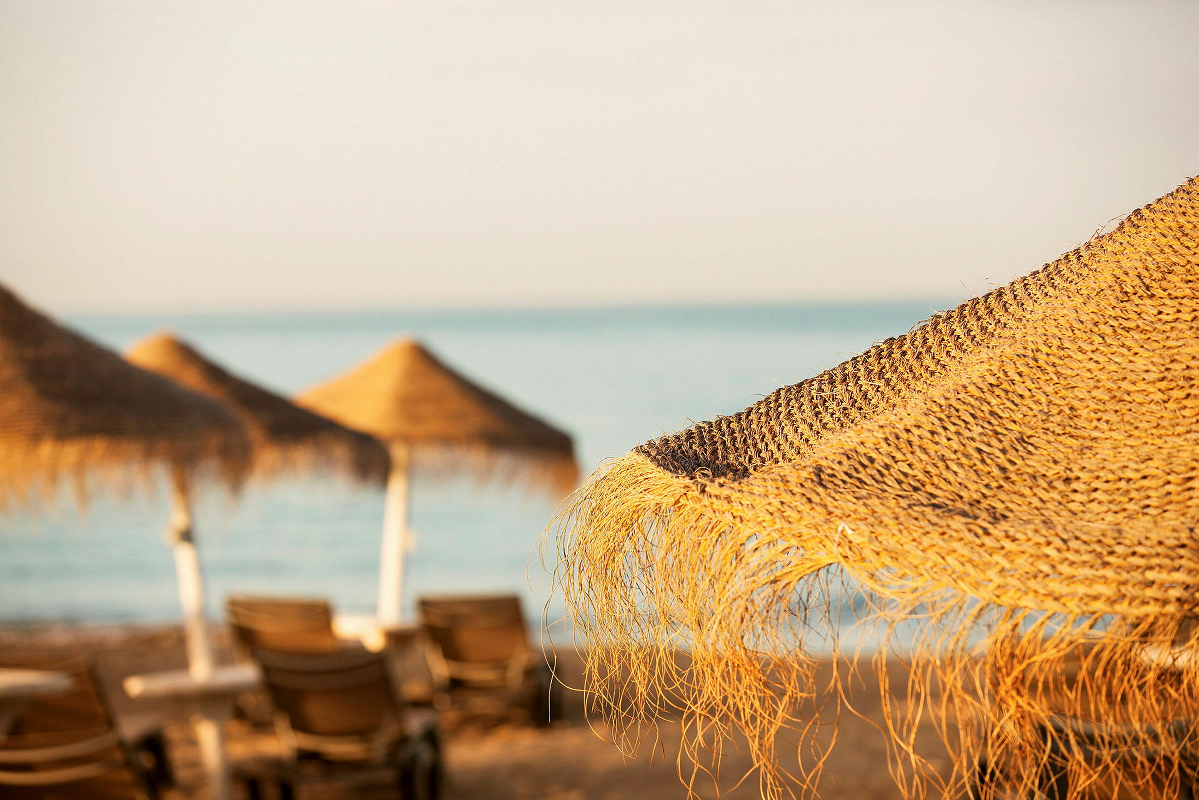 Stranden med parasoller i halm och solstolar. (AI-genererad text)