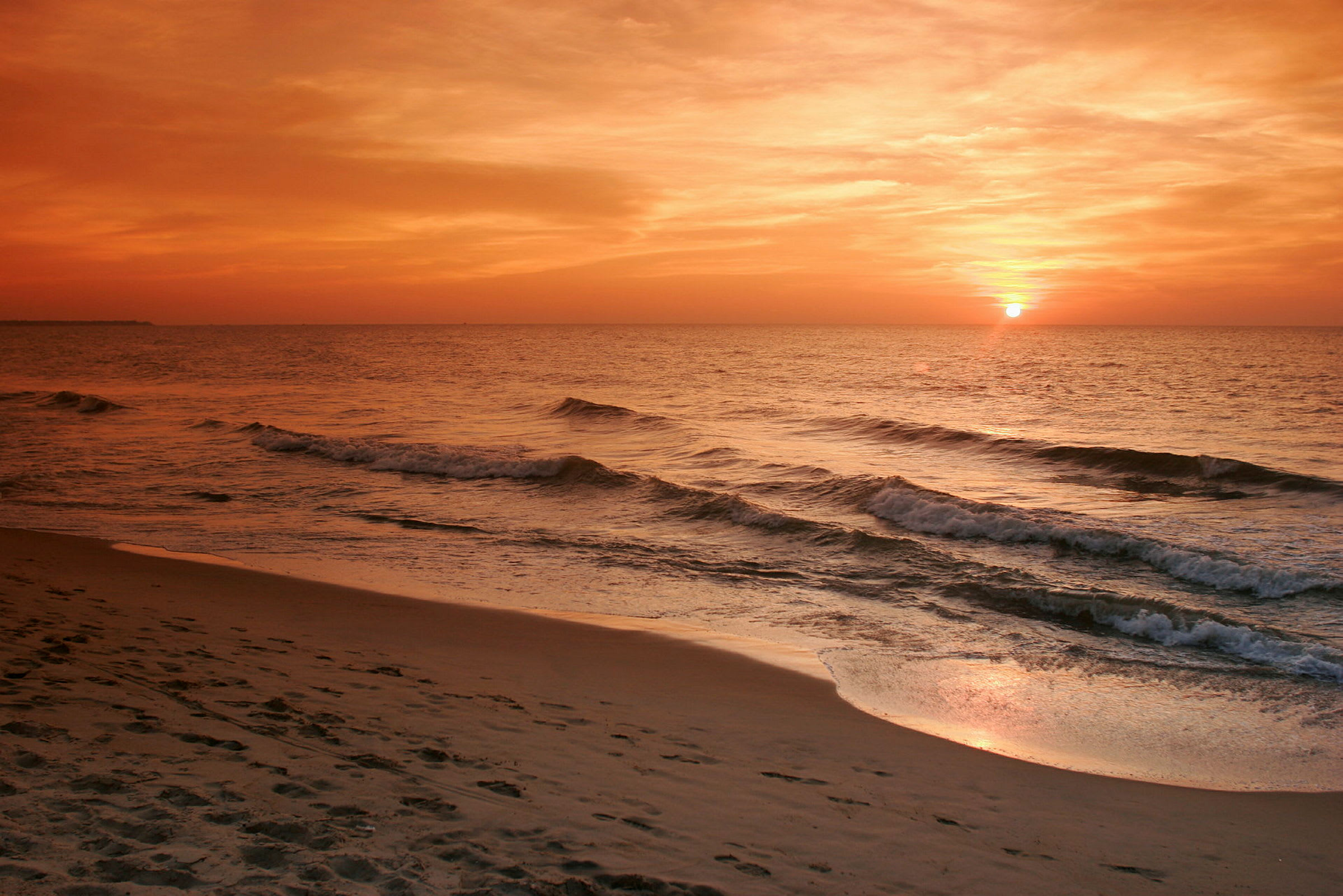 Bild föreställande en strand vid havet med vågor och en solnedgång. (AI-genererad text)
