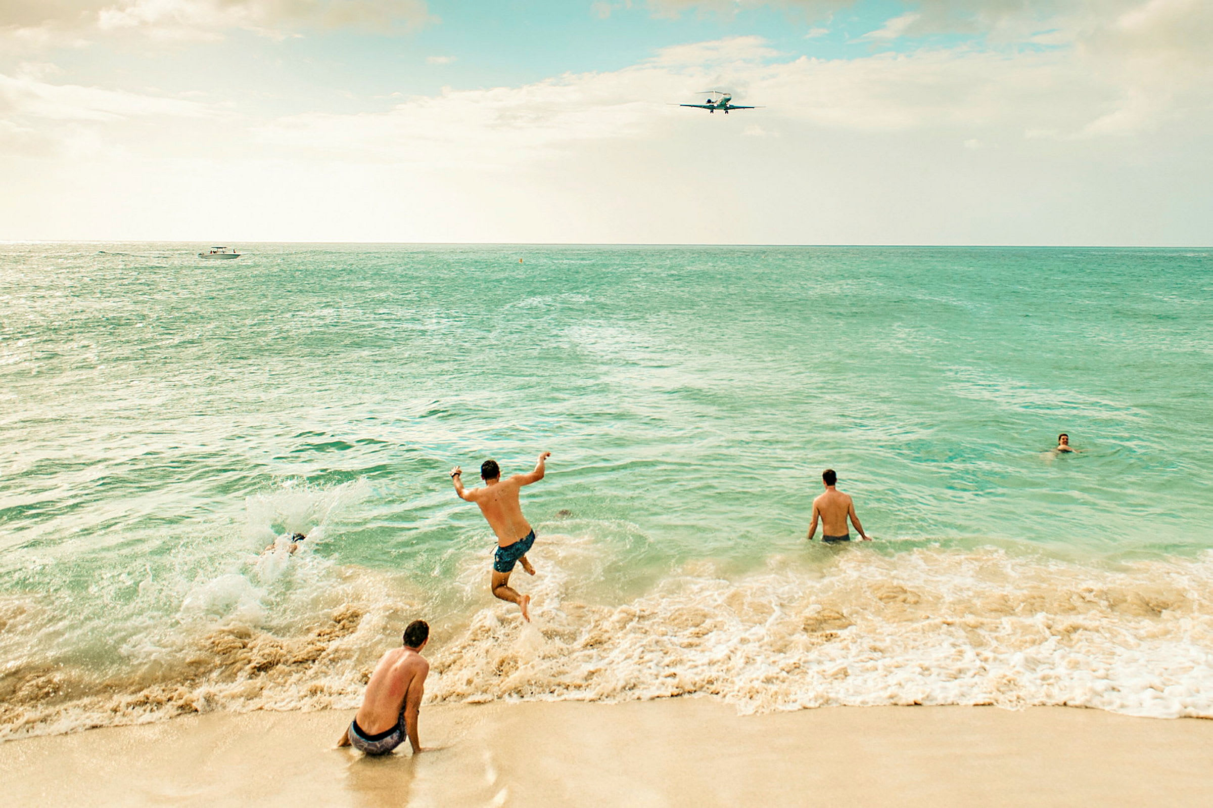 Personer leker i vattnet vid en sandstrand, och ett flygplan syns på himlen. (AI-genererad text)
