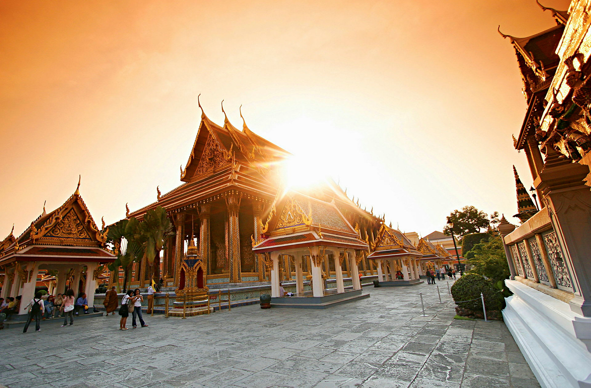 Bilden visar ett thailändskt tempel med dekorerade tak och byggnader i solnedgångens ljus. (AI-genererad text)