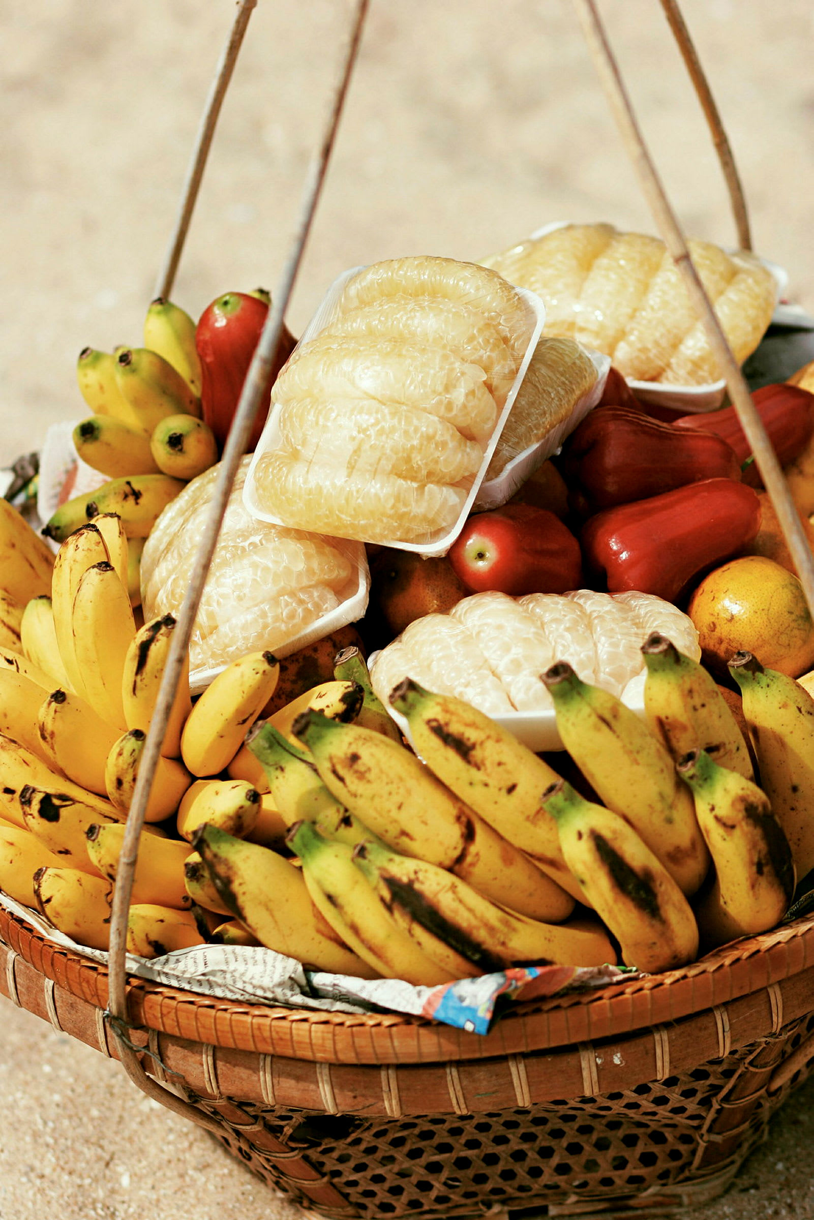 En korg fylld med olika asiatiska frukter som bananer, röd frukt och skalade pomelo. (AI-genererad text)