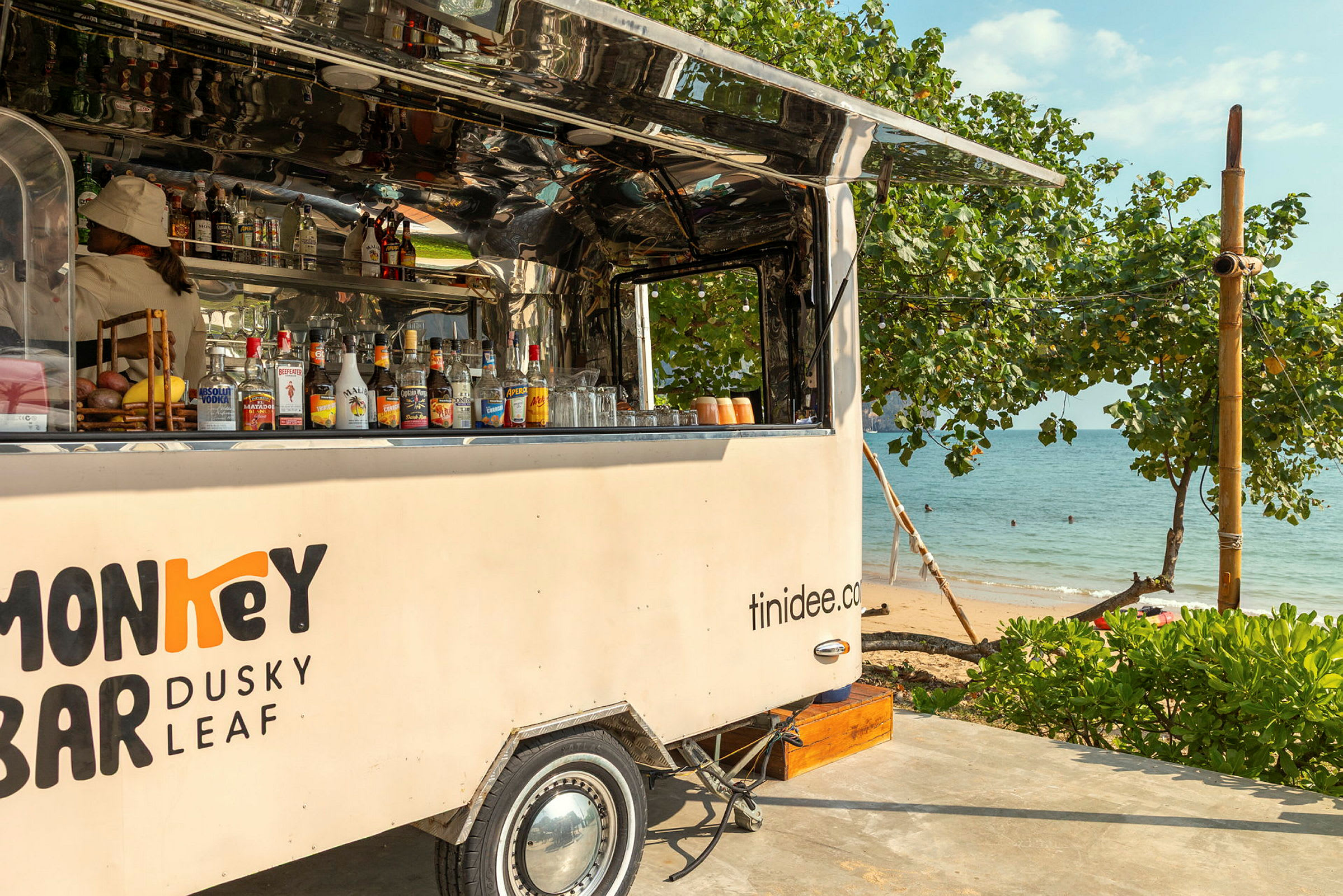 Mobil bar uppställd vid stranden, omgiven av grönska och hav i bakgrunden. (AI-genererad text)