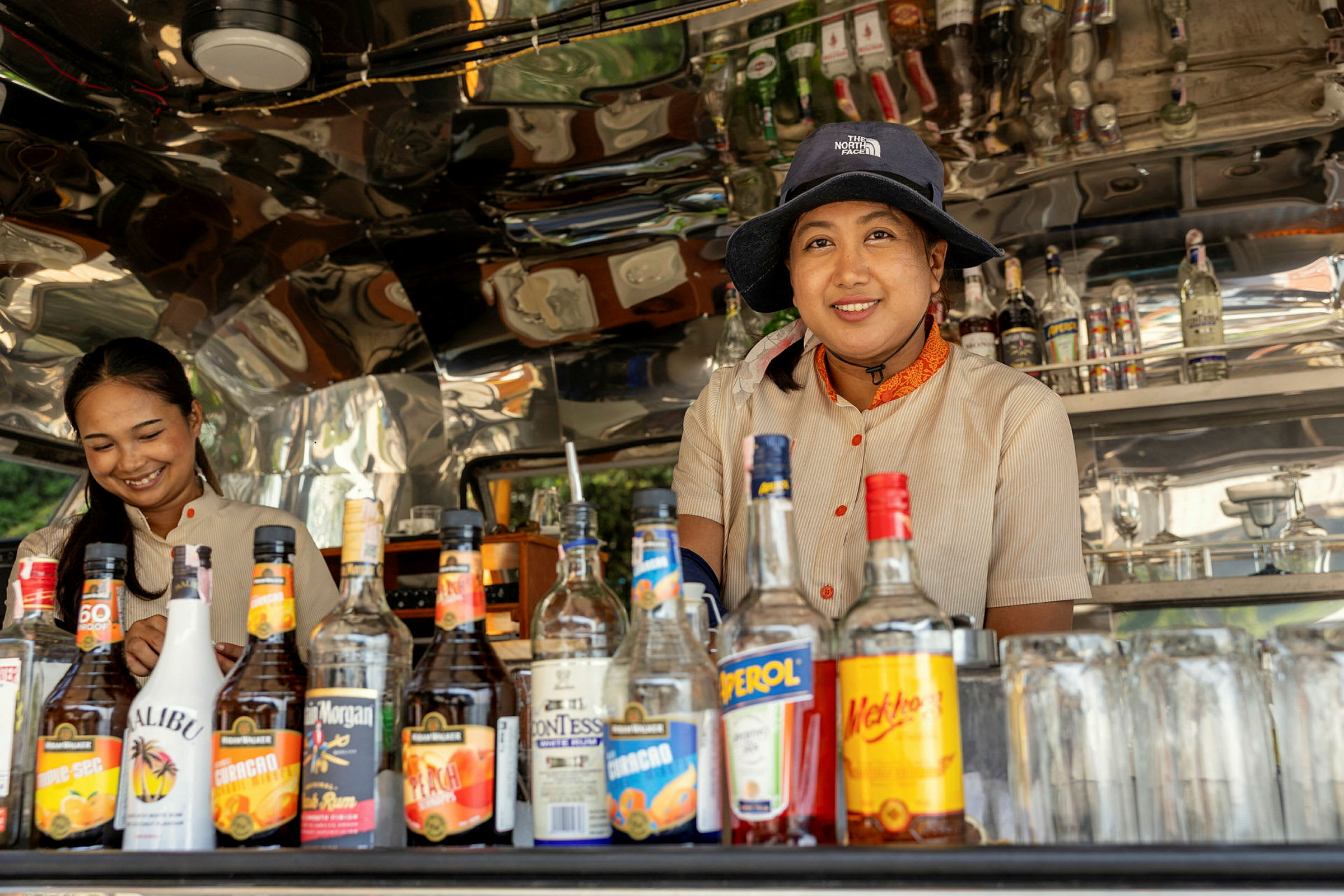 Två personer står bakom en bar med flaskor och glas runt omkring. (AI-genererad text)