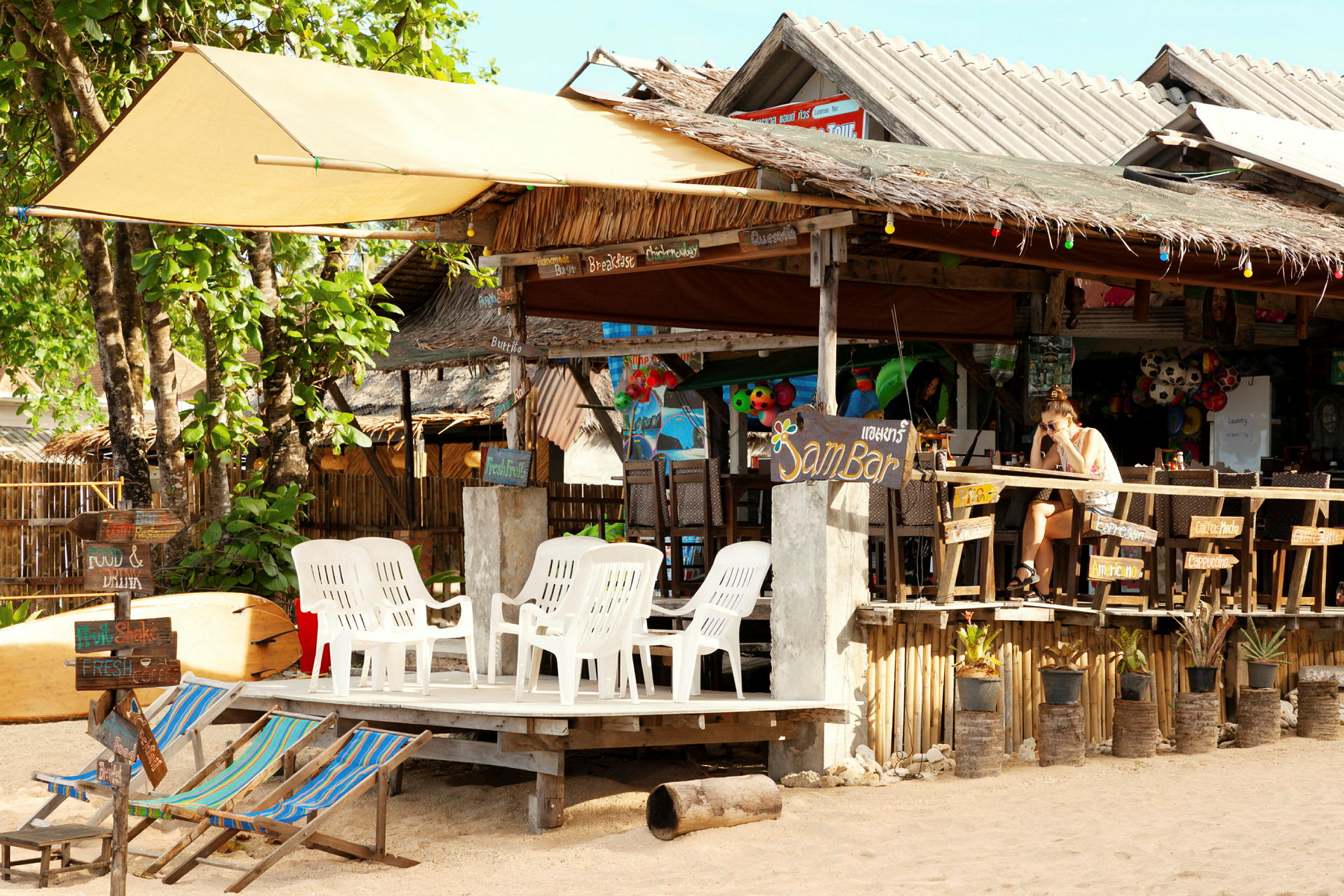 Ett café vid stranden med plaststolar och färgglada dekorationer. (AI-genererad text)