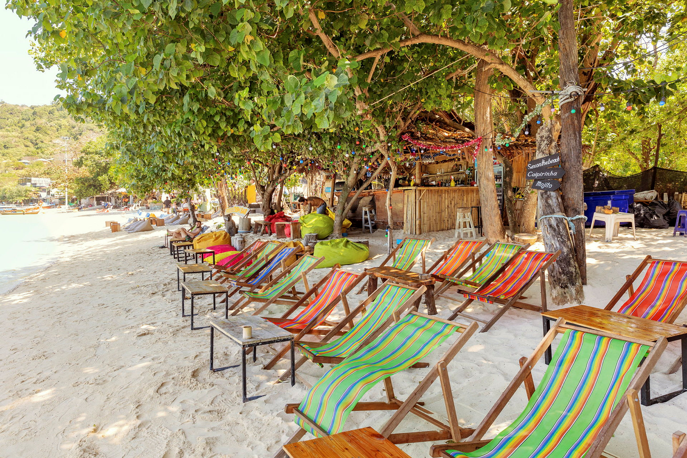 Strand med färgglada solstolar och ett trädkantat café i bakgrunden. (AI-genererad text)