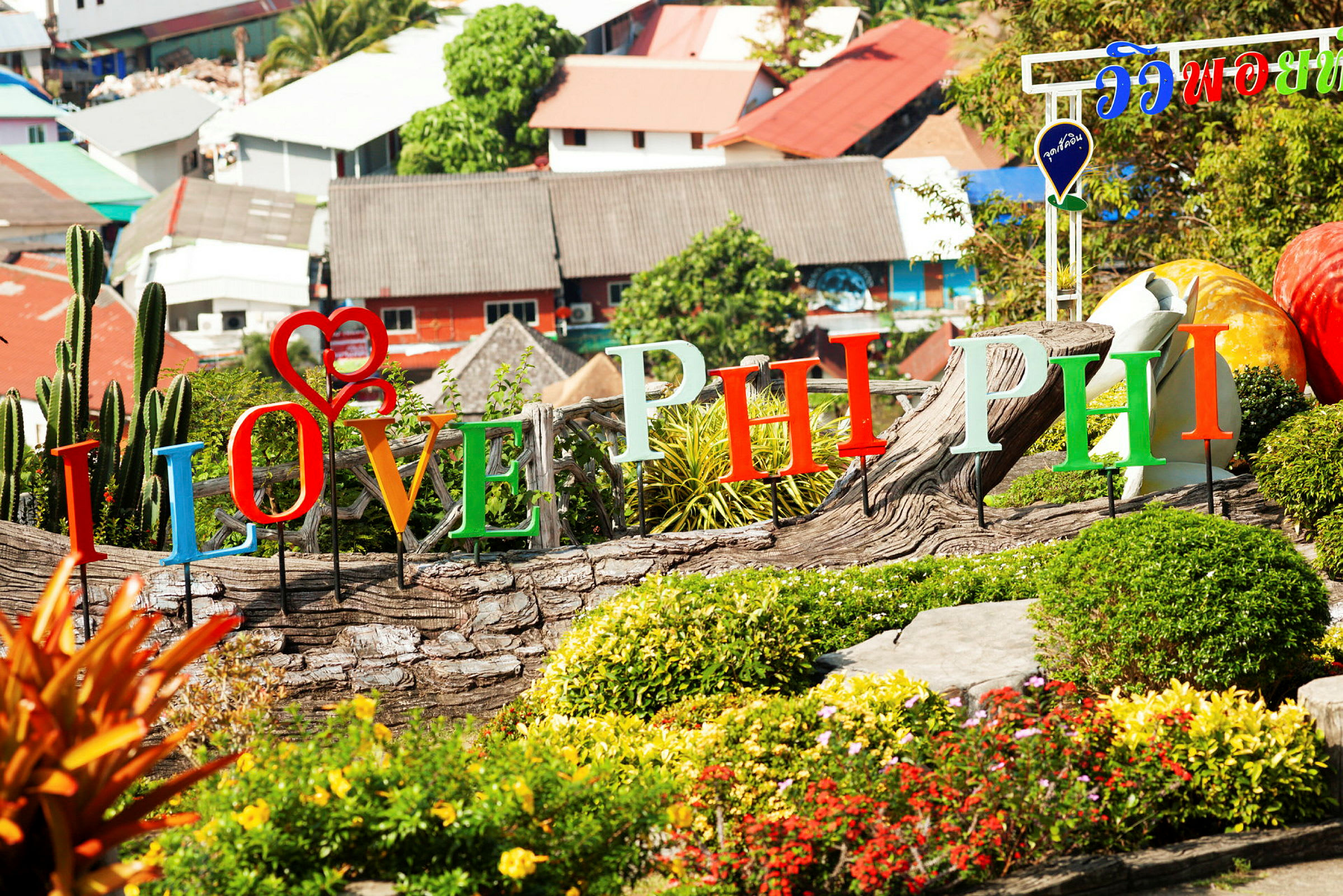 Färgglada bokstäver som stavar "I Love Phi Phi" är placerade i ett trädgårdsområde med buskar och blommor. (AI-genererad text)