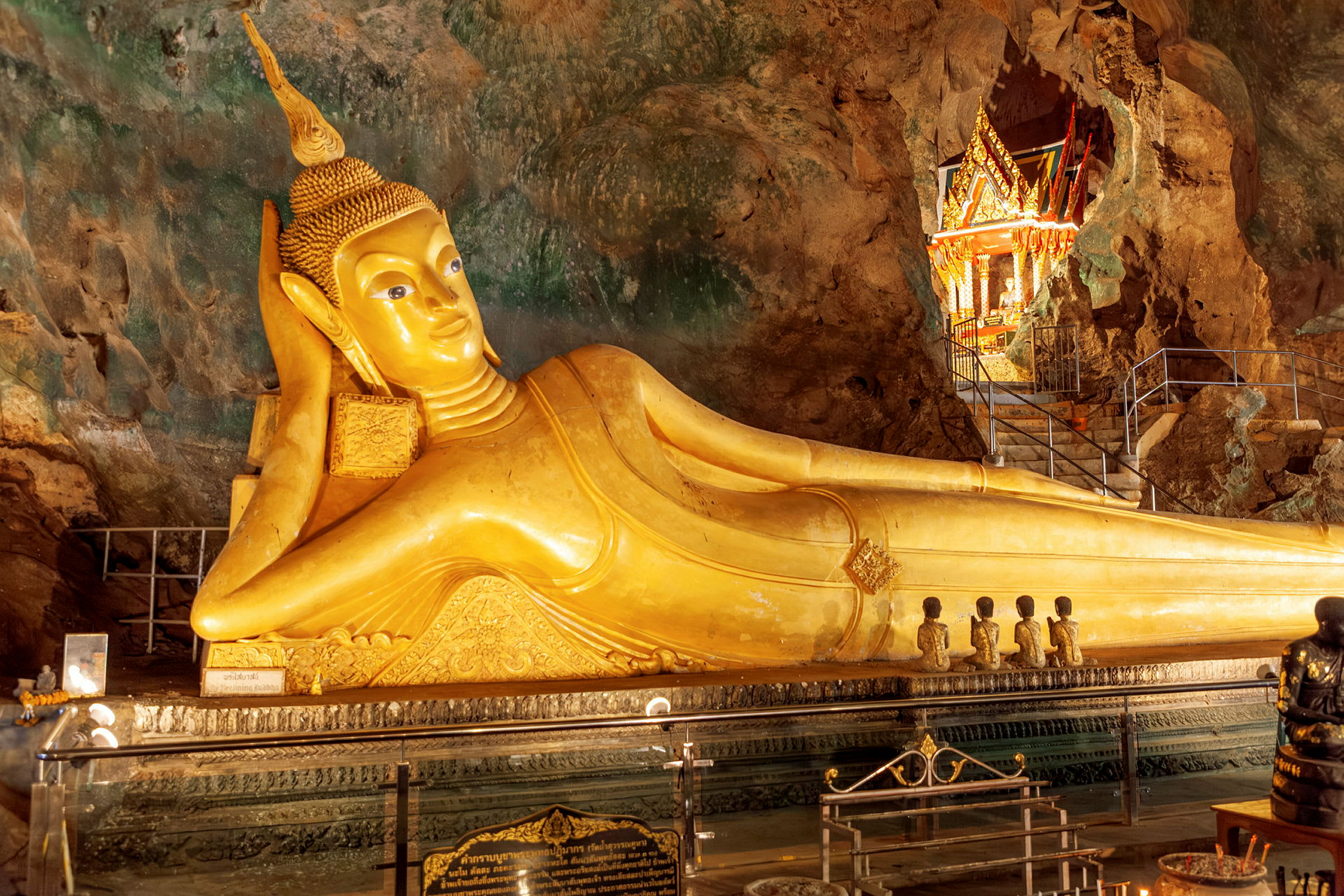 En gyllene liggande staty av Buddha inuti en klippa, omgiven av ett vackert dekorerat område med detaljerade dekorationer. (AI-genererad text)
