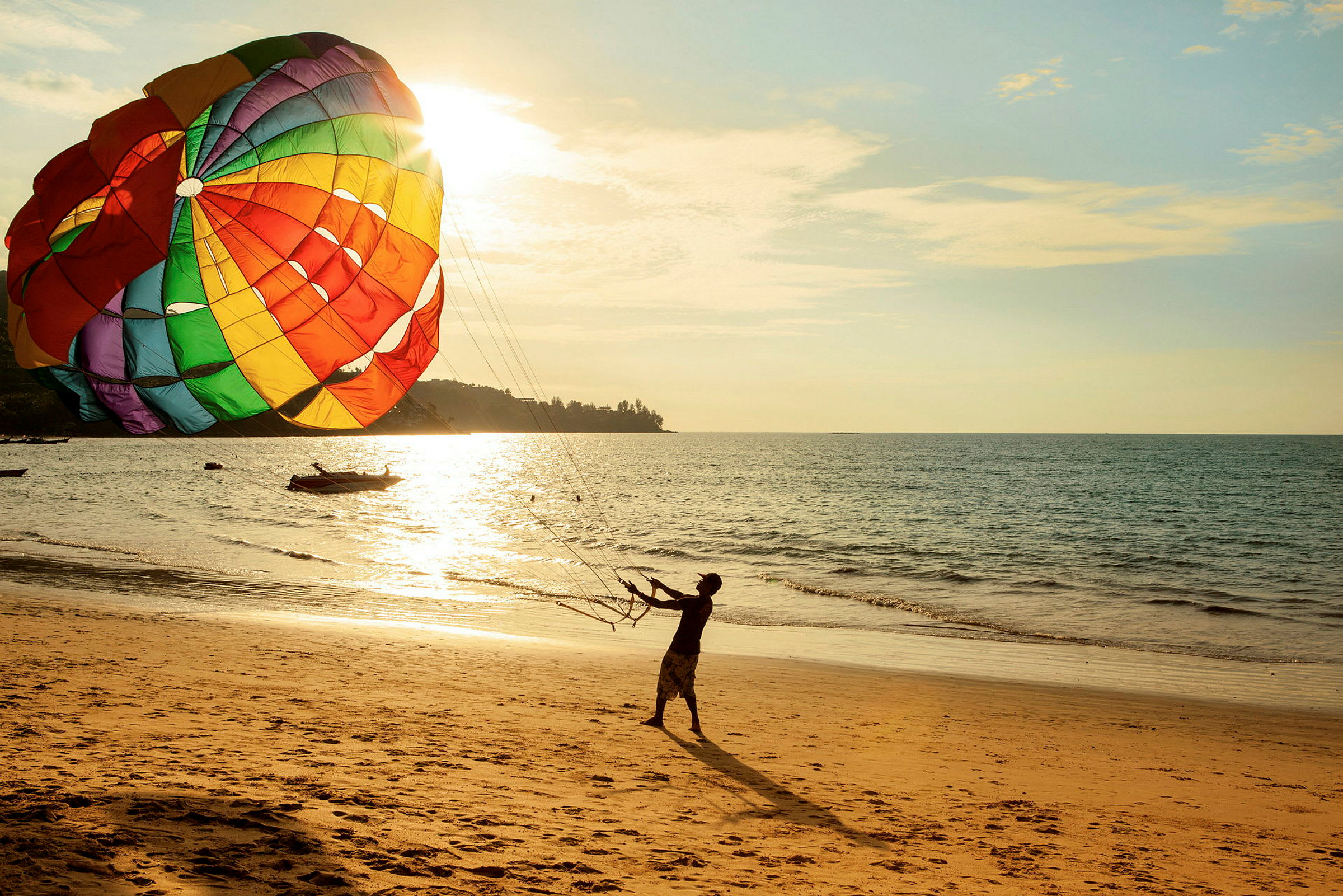 Person håller i linor till en stor färgglad parasail på en solbelyst strand. (AI-genererad text)