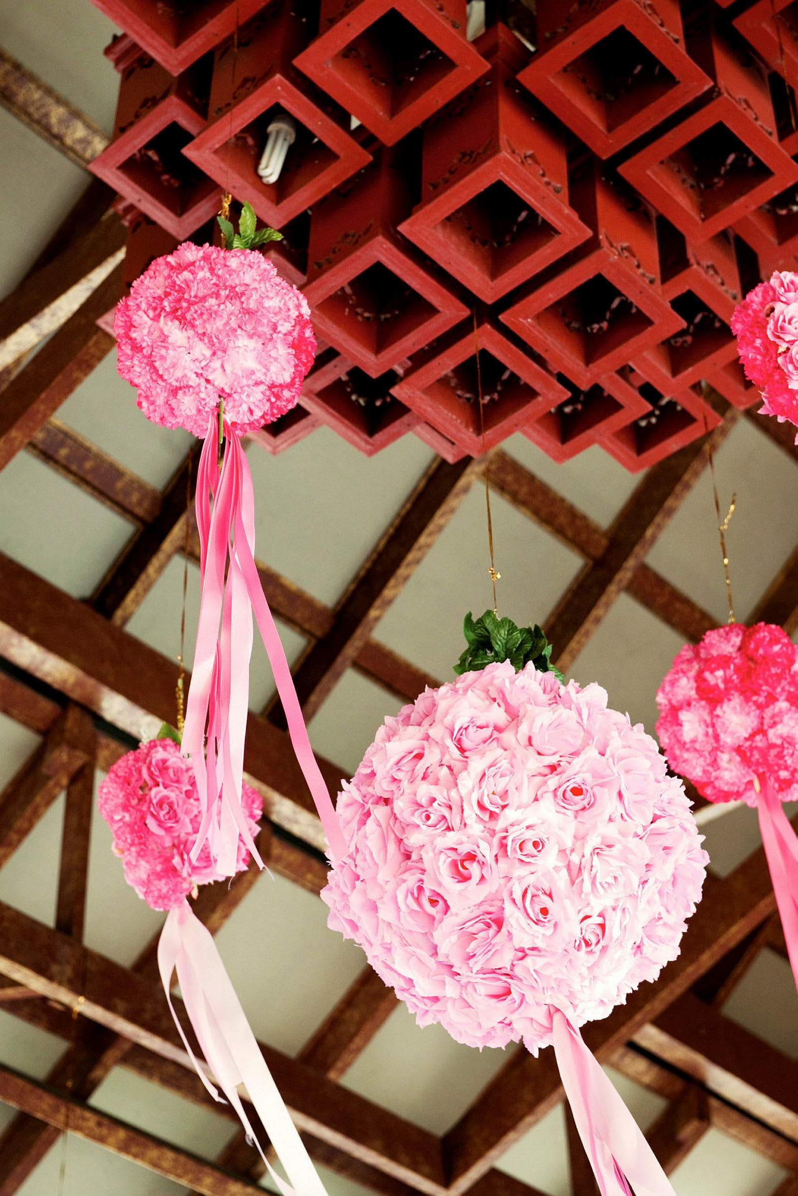 Dekorativa bollar av rosa blommor med hängande band i rosa och vita färger, upphängda från en takstruktur. (AI-genererad text)