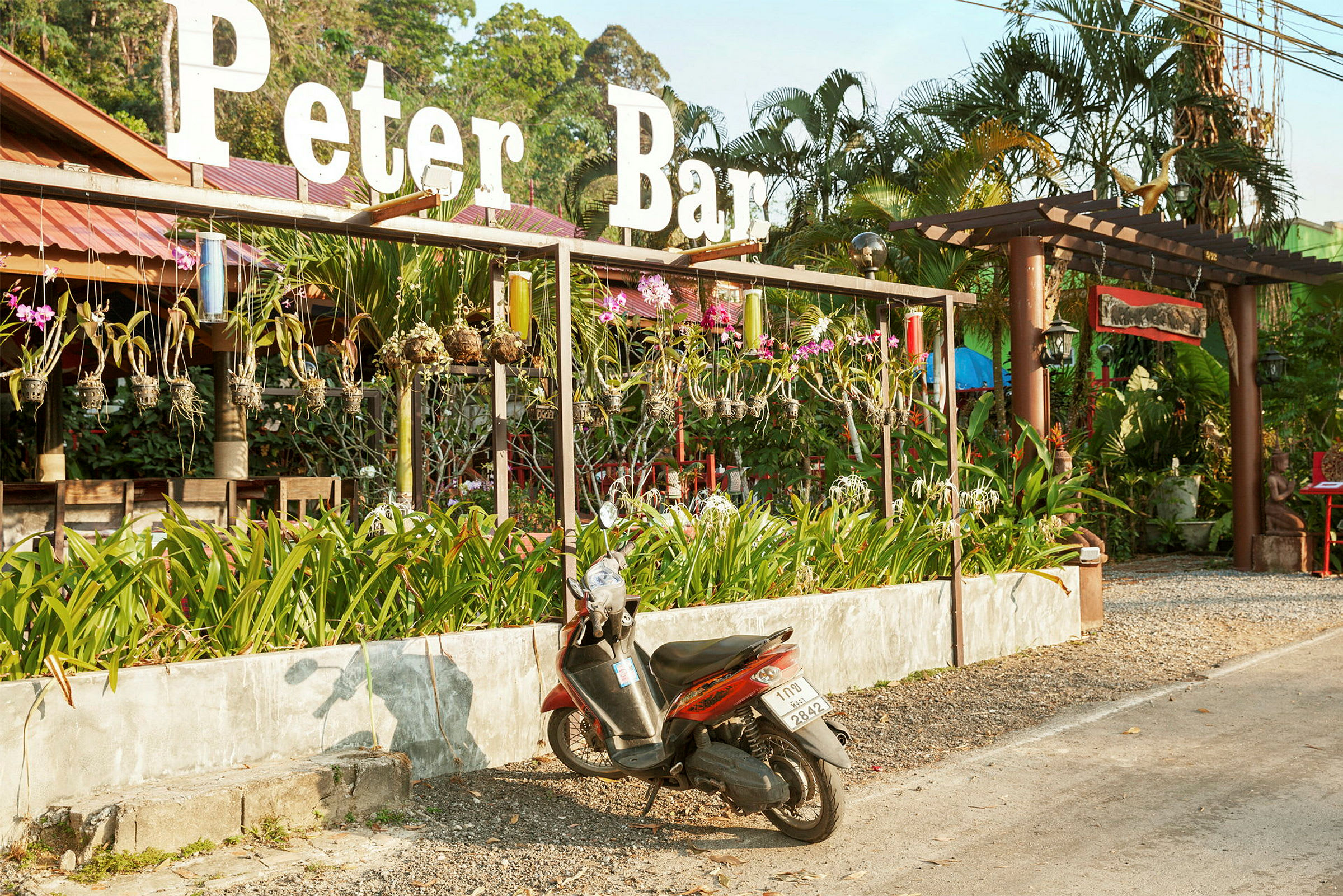 En motorcykel parkerad framför en restaurang med skyltar och grönska. (AI-genererad text)