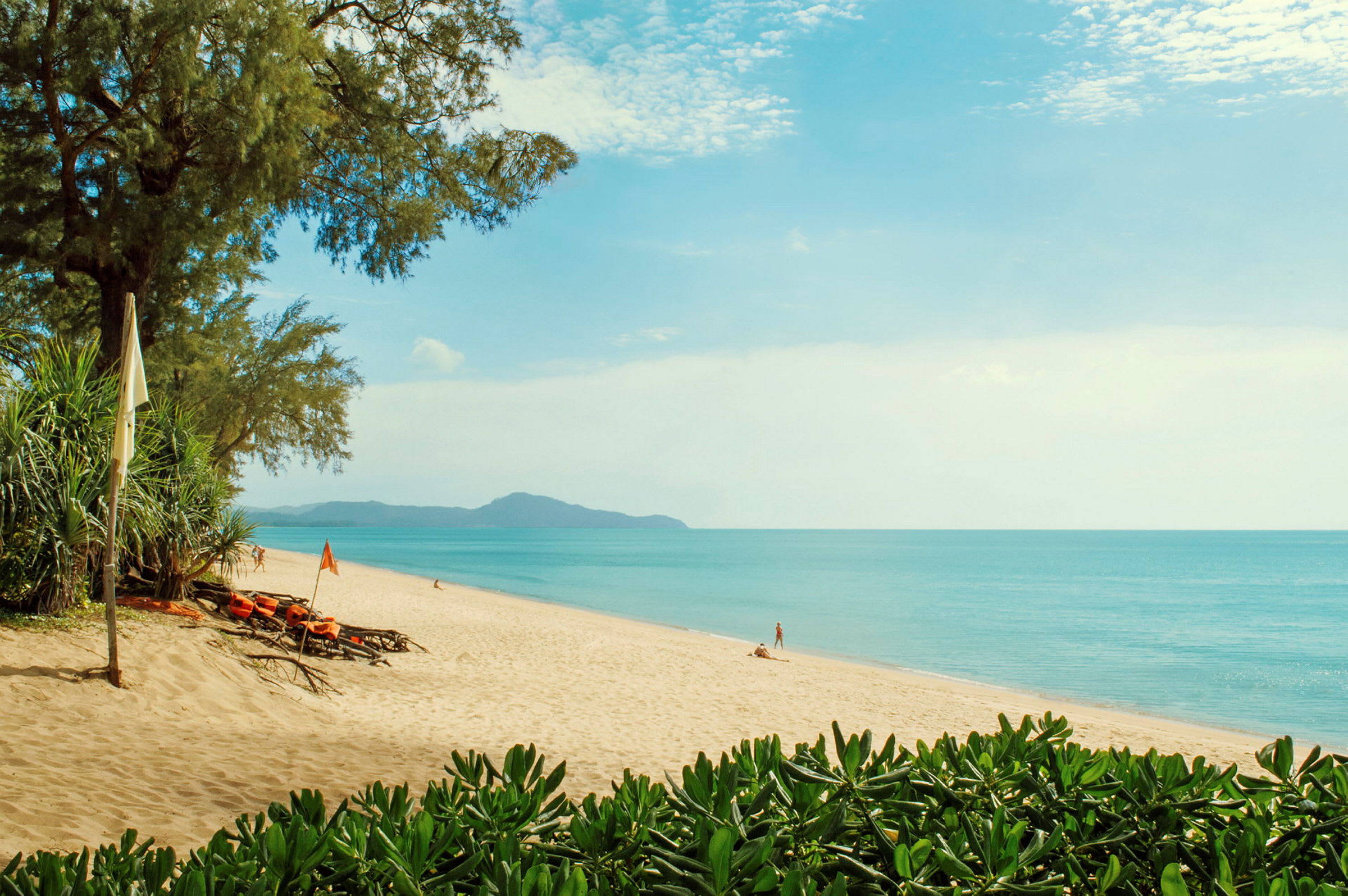 Vid Mai Khao Beach på Phuket möts du av turkosblått hav, en lång sandstrand och grönskande träd längs kusten.
