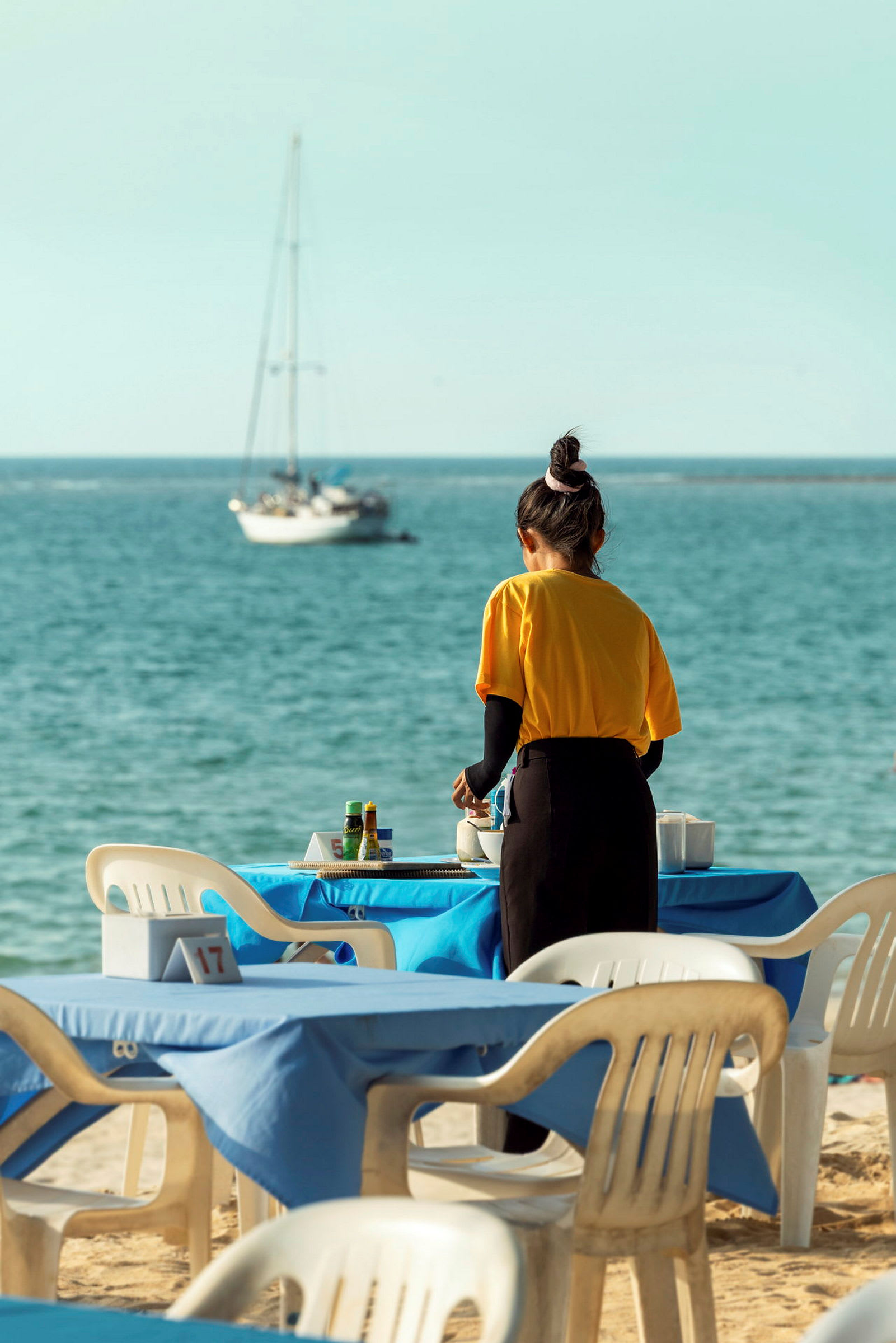 En person ordnar bord på en restaurang med utsikt över havet. (AI-genererad text)