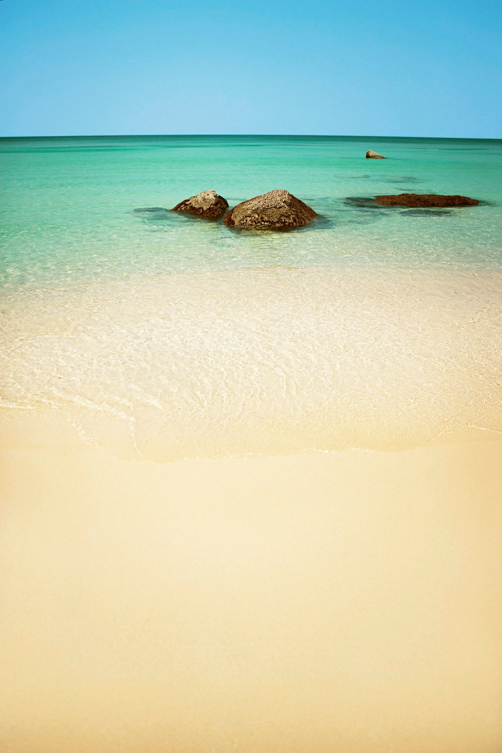 En sandstrand med klart vatten och några synliga stenar i havet. (AI-genererad text)
